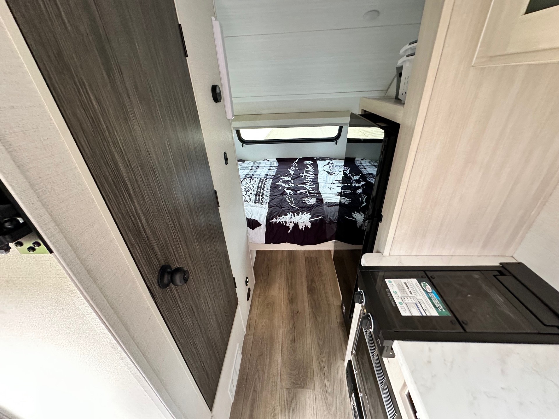 RV rental interior featuring a hallway leading to a cozy bedroom with a window, and a compact kitchenette on the right.. Forest River RPod 2026