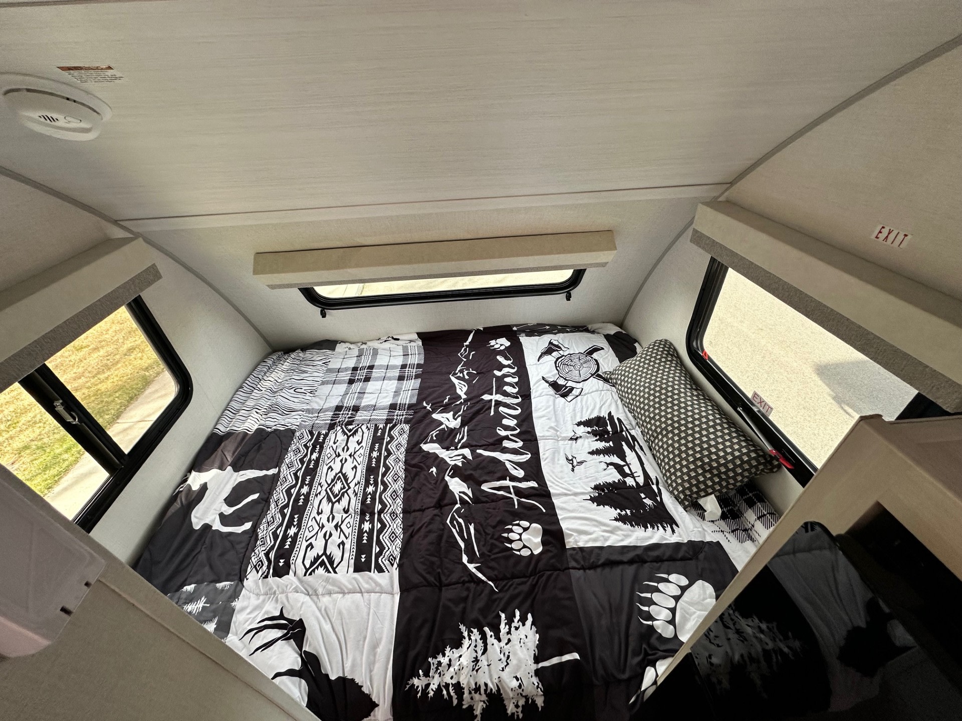 Cozy RV rental sleeping area with an adventure-themed bed, windows, and a smoke detector on the ceiling.. Forest River RPod 2026
