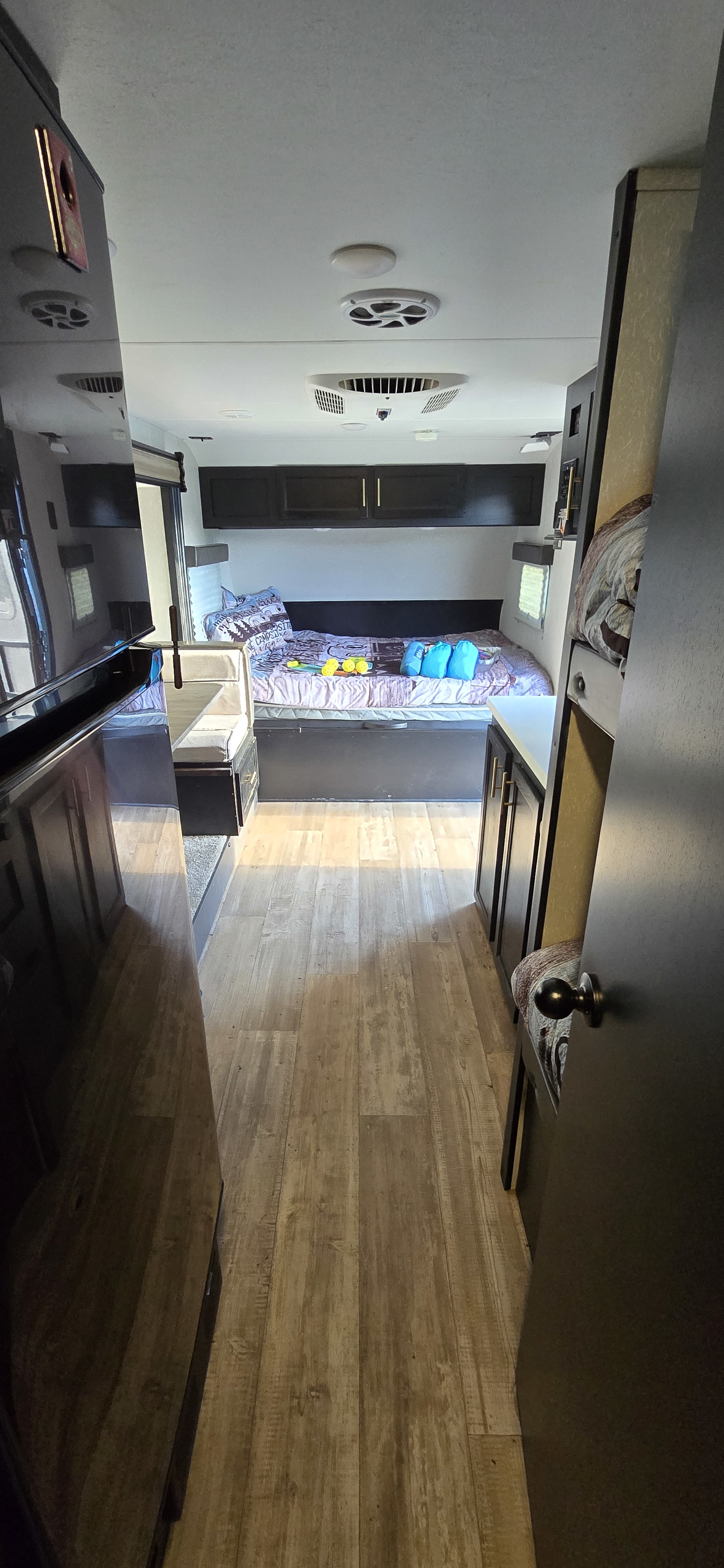 RV rental interior: bed with storage, dinette, overhead cabinets, wood-look floor, and bunk beds on the right.. Forest River Cherokee Wolf Pup Black Label 2021