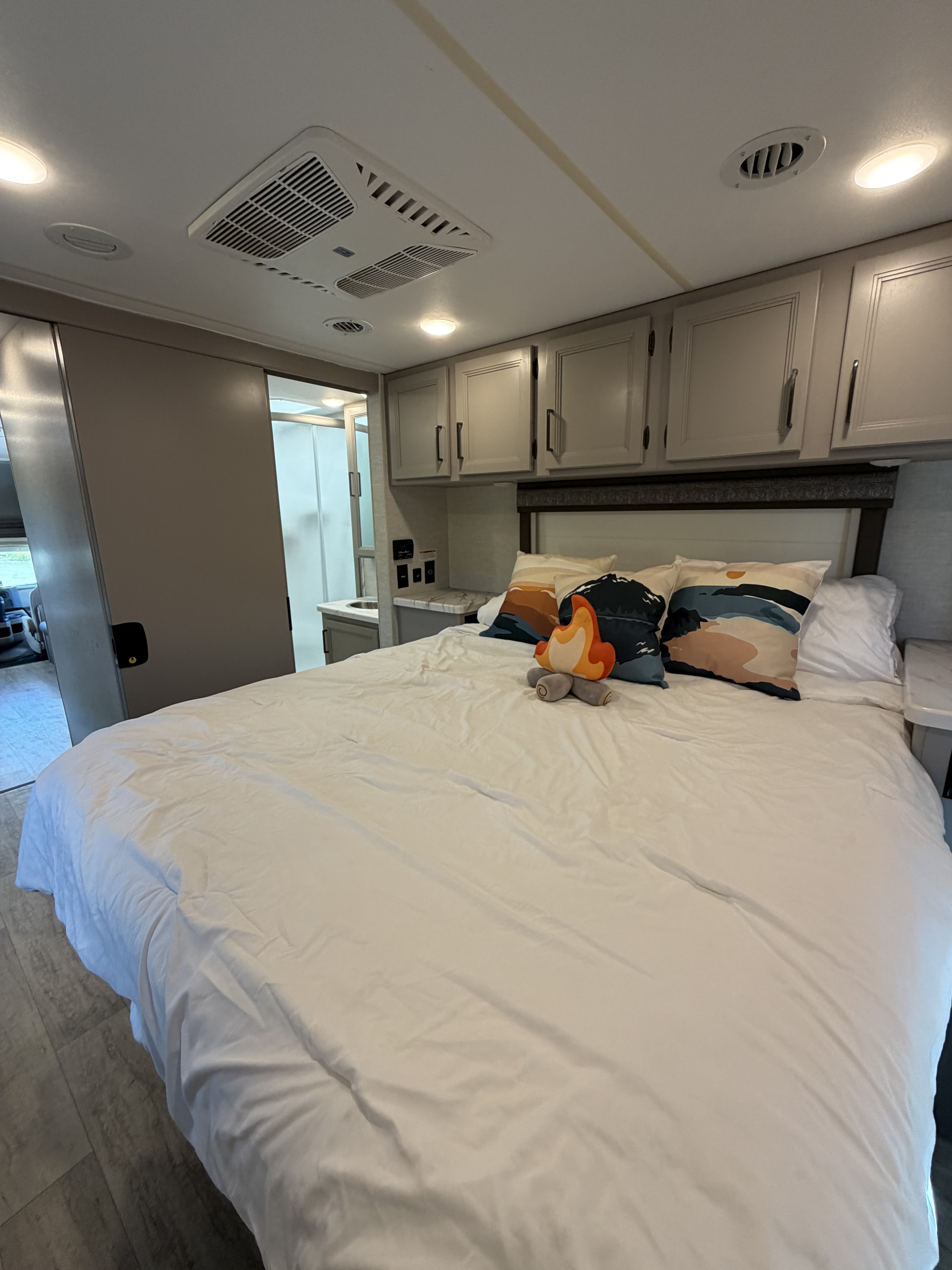 Modern rv rental bedroom with white bedding, cozy pillows, overhead cabinets, and an ensuite bathroom.. Thor Chateau 2024