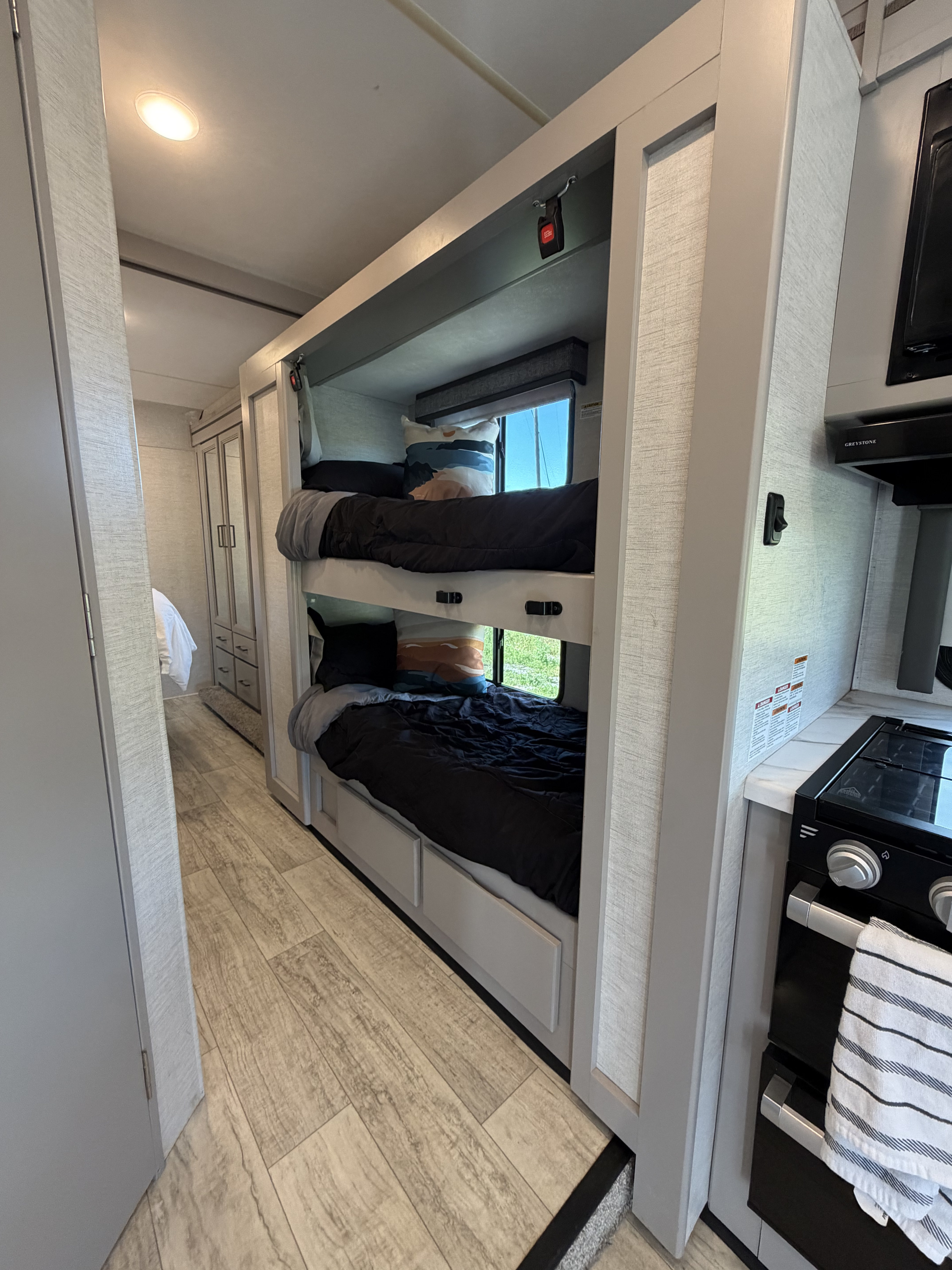 This RV rental features bright, modern bunk beds with windows, a compact kitchen, and a hallway leading to other rooms.. Thor Chateau 2024