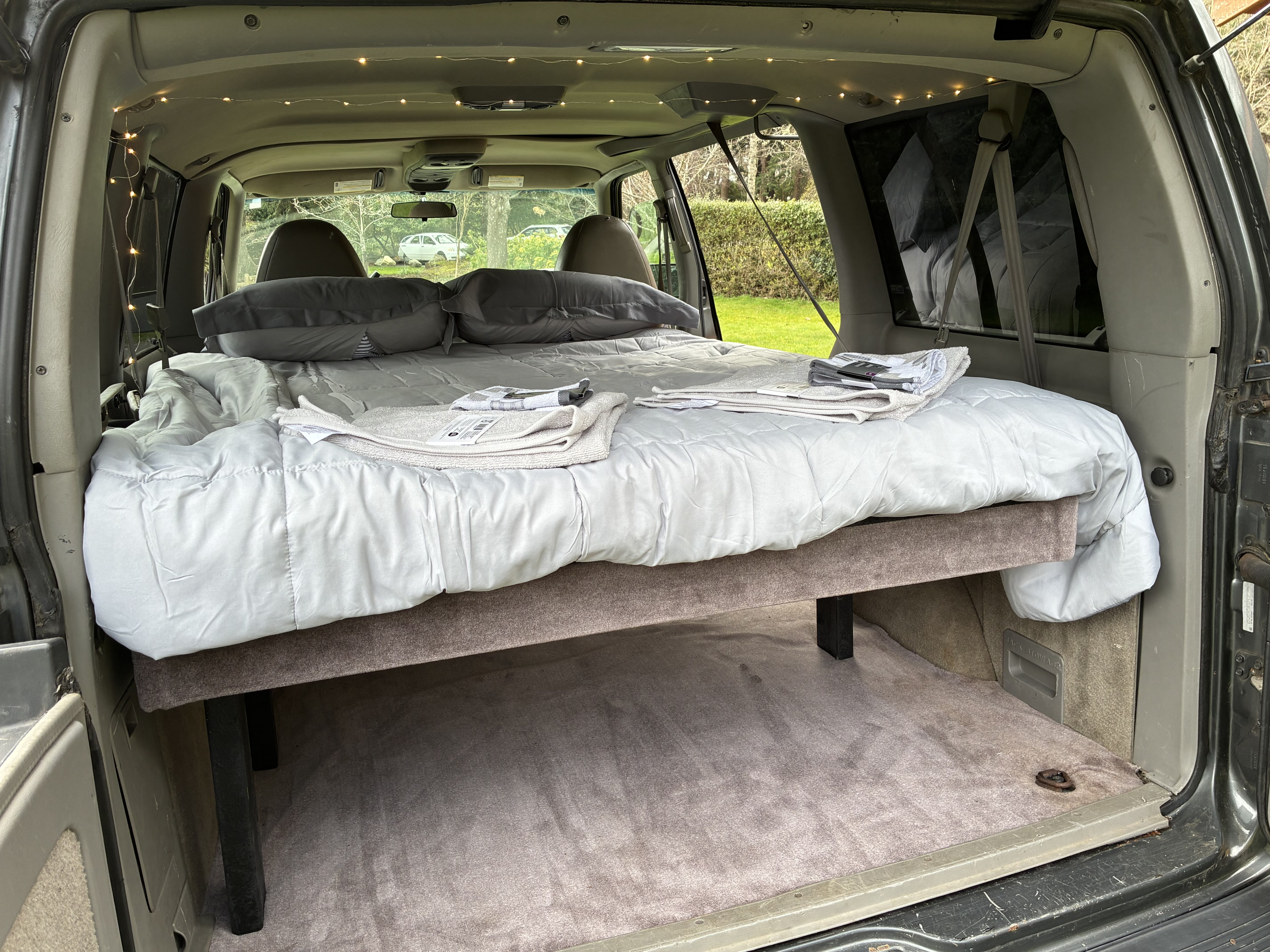 Relaxing RV rental sleep setup in a converted van, complete with fairy lights, comfy bed, & under-bed storage.. Gmc Safari 2000