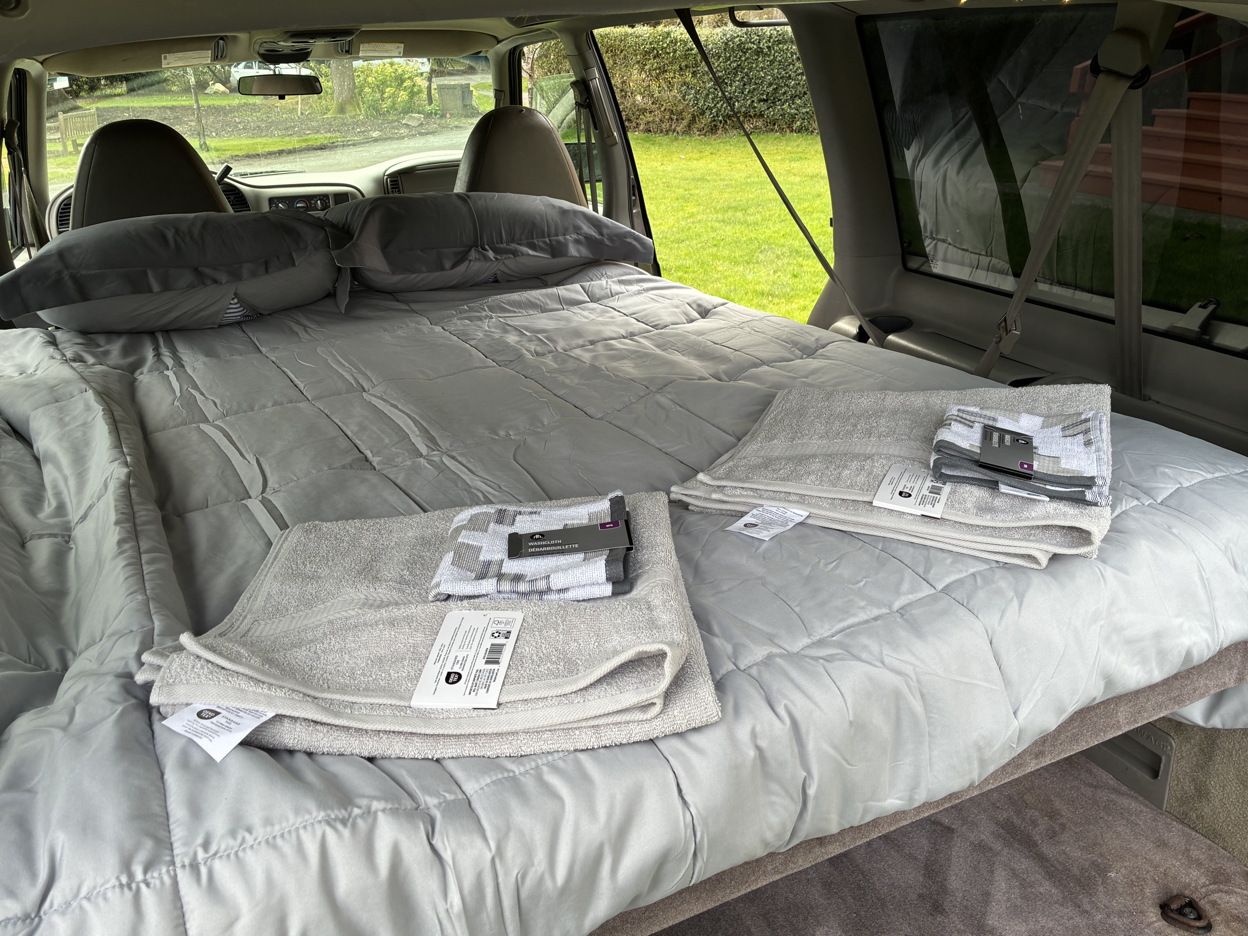 RV rental: Comfortable sleeping setup in a van, featuring a quilted comforter, pillows, and fresh towels.. Gmc Safari 2000