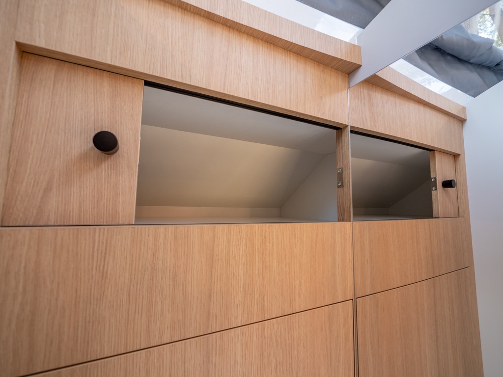 Light-toned wooden cabinetry features sliding doors revealing angled storage compartments, perfect for an RV rental.. Ford Transit 2024