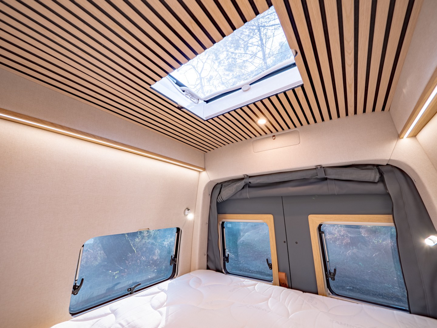 Modern rv rental interior: wooden-slat ceiling, skylight, side windows, LED lighting, & comfortable bed for adventures.. MAN TGE 4x4 2025