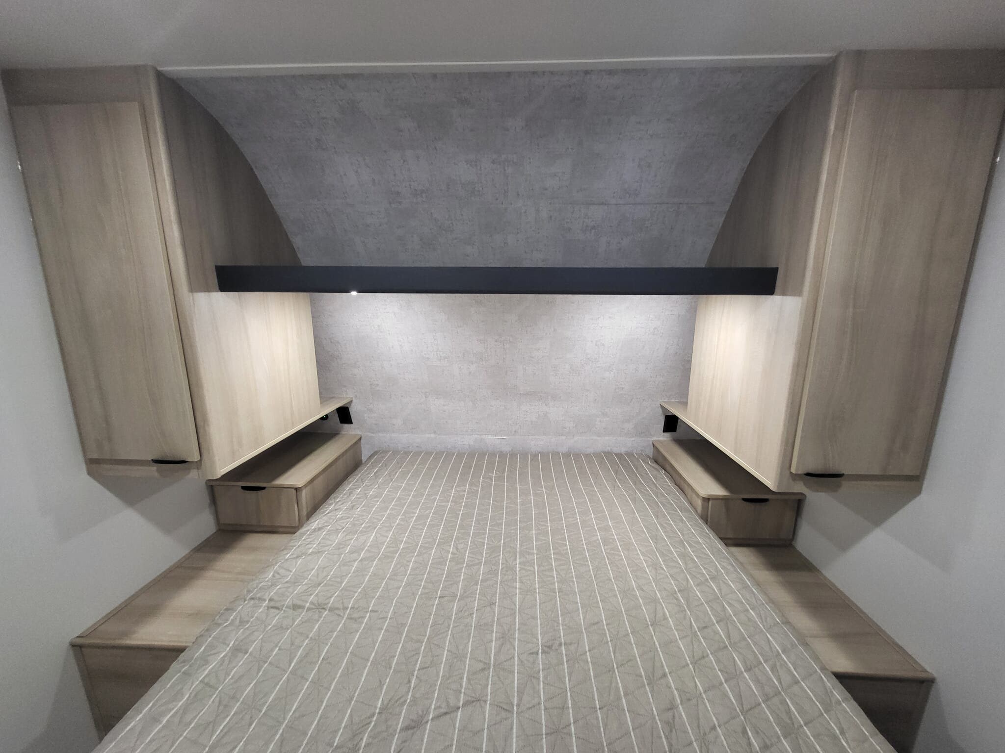 Modern RV rental bedroom featuring a striped bed, integrated nightstands, and overhead storage cabinets. Bright, compact, and functional space.. Winnebago Minnie Winnie 2023