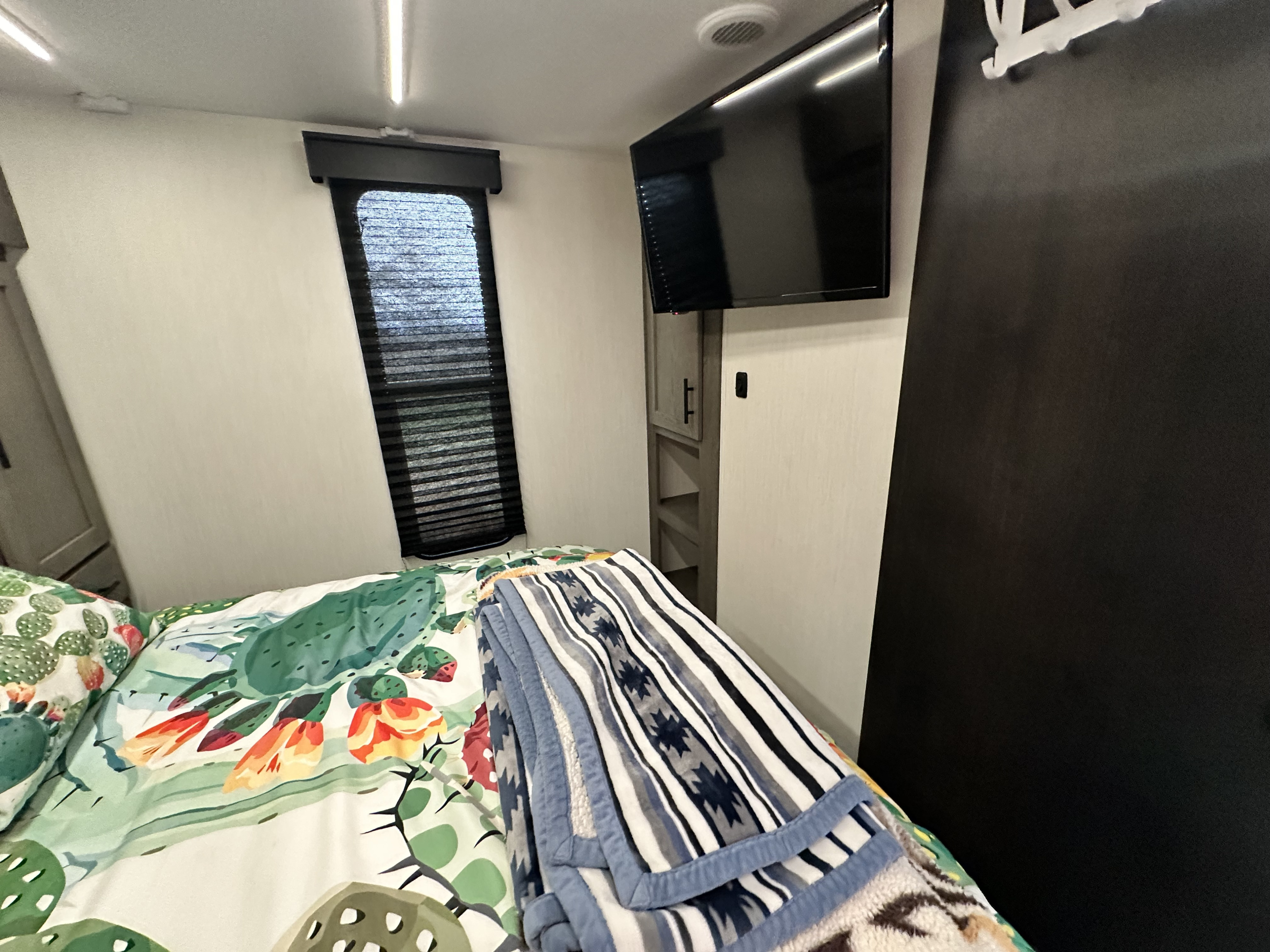 Compact and comfortable RV rental bedroom, featuring a vibrant cactus-themed bed, window, and wall-mounted TV.. Forest River Cherokee Alpha Wolf 2025
