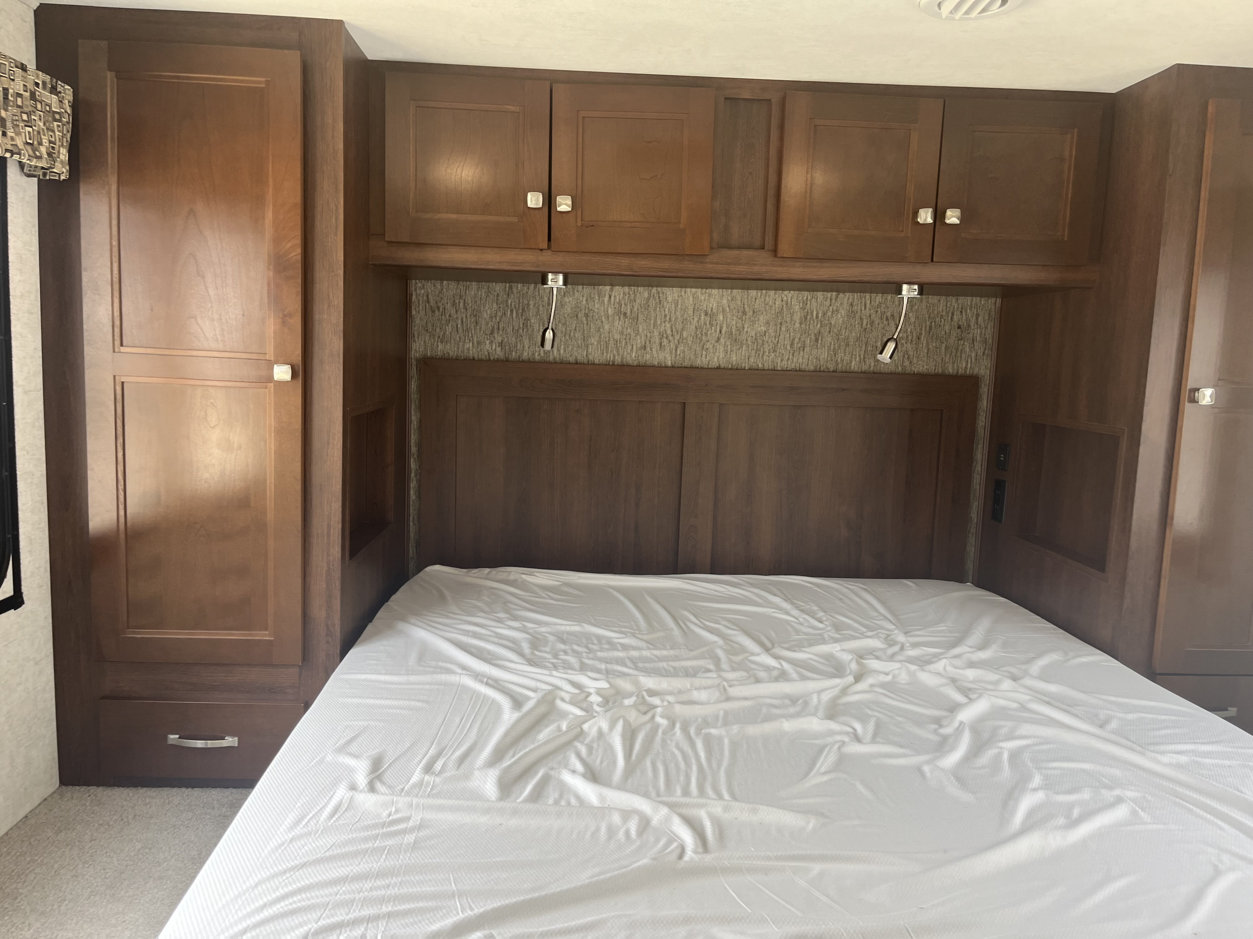 Cozy RV rental bedroom with a white bed, dark wood cabinets, built-in storage, and reading lights.. Forest River Sunseeker 2018
