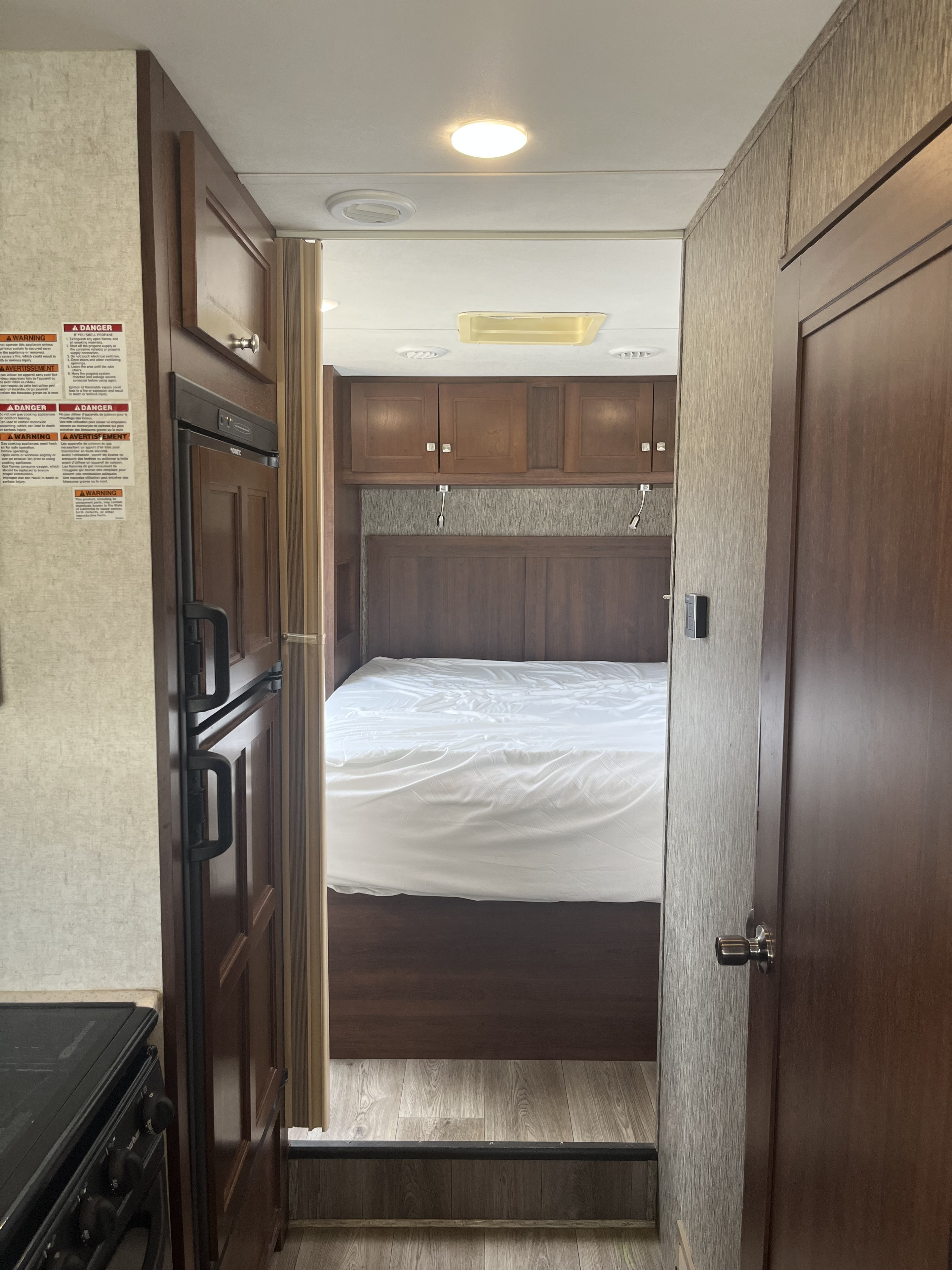 RV rental interior: View into a compact bedroom with a bed and cabinets, seen from the kitchen area with a fridge.. Forest River Sunseeker 2018