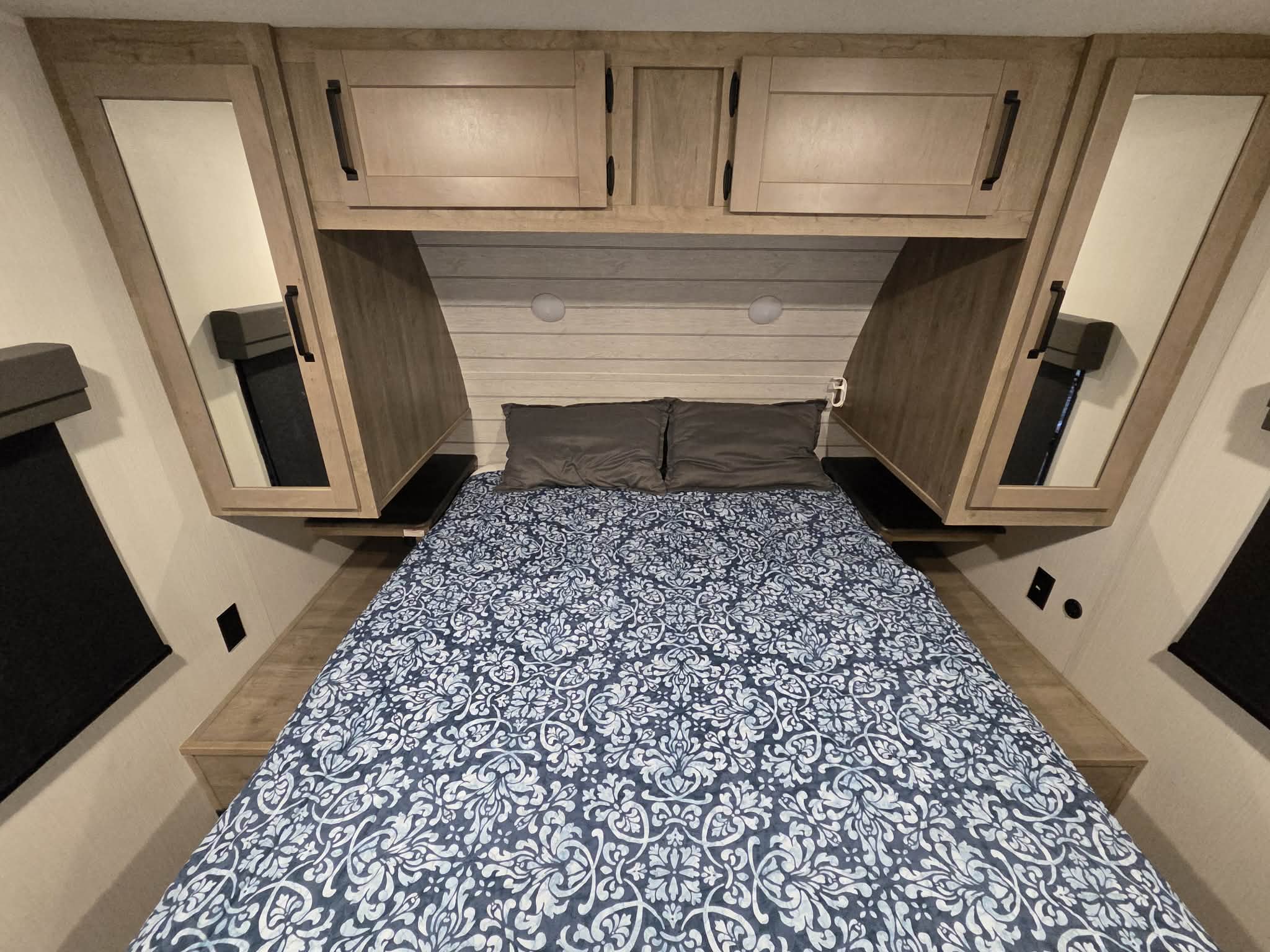 Cozy RV rental bedroom with a blue patterned comforter, overhead cabinets, and bedside storage. Ideal for travel.. Forest River Palomino Puma 2024