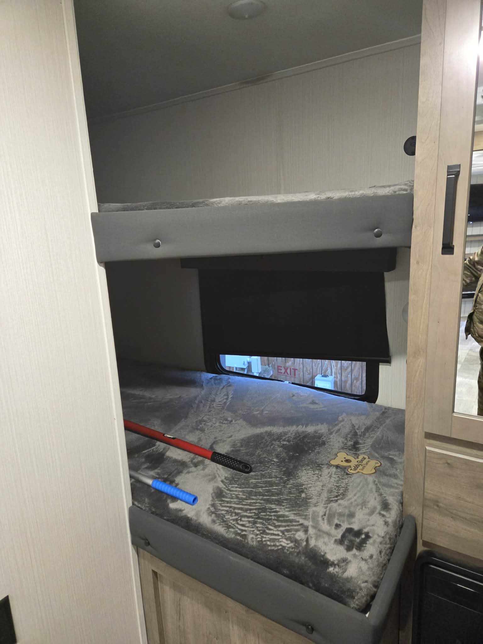 Inside this rv rental, bunk beds are visible. The lower bunk has a textured mattress, window, and cleaning tools.. Forest River Palomino Puma 2024