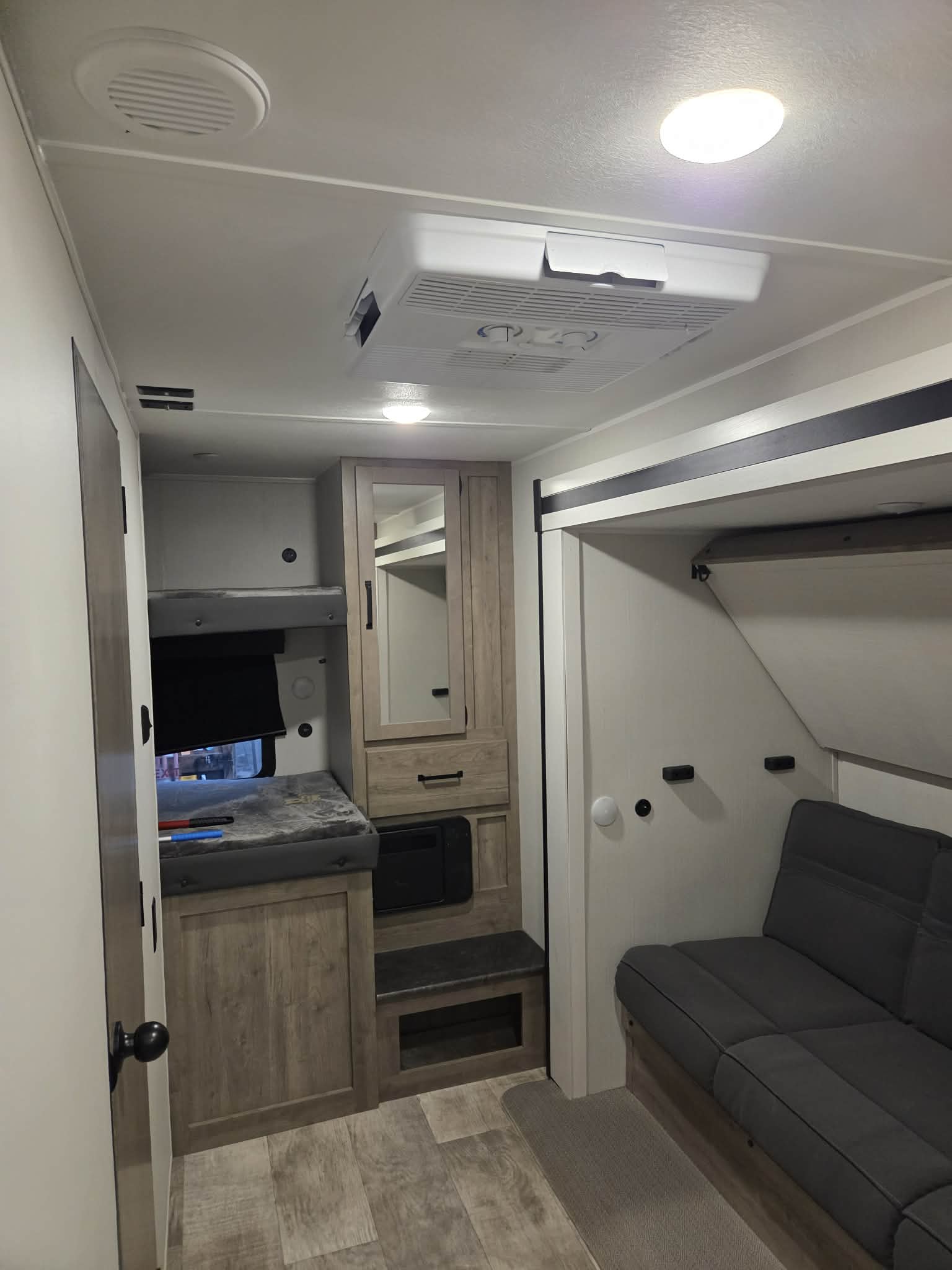 Inside an RV rental, showing bunk beds on the left, a mirrored cabinet, and a gray sofa on the right. Ceiling has AC and lights.. Forest River Palomino Puma 2024