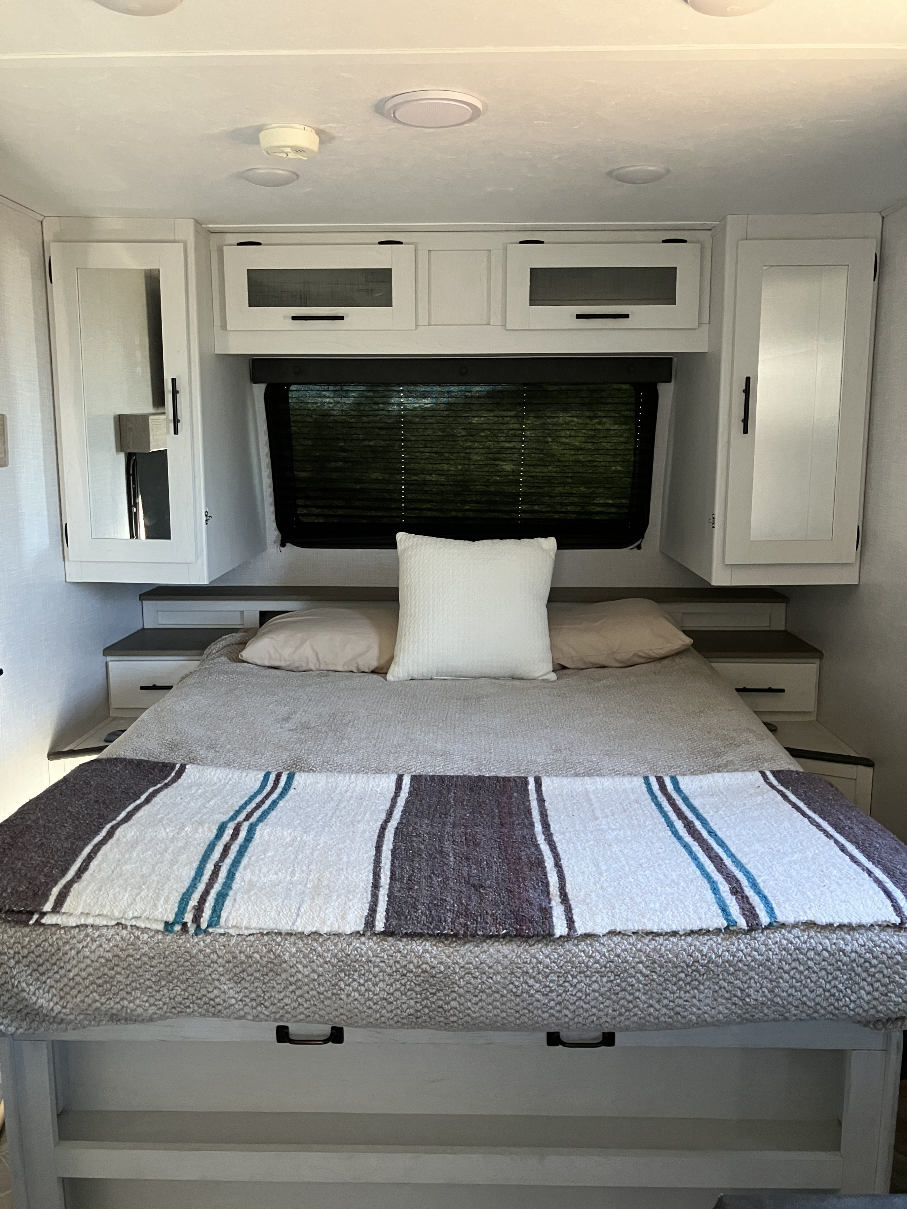 Inside an RV rental: a modern bedroom with a comfortable bed, convenient overhead cabinets, and a window.. Forest River Coleman Rubicon 2023