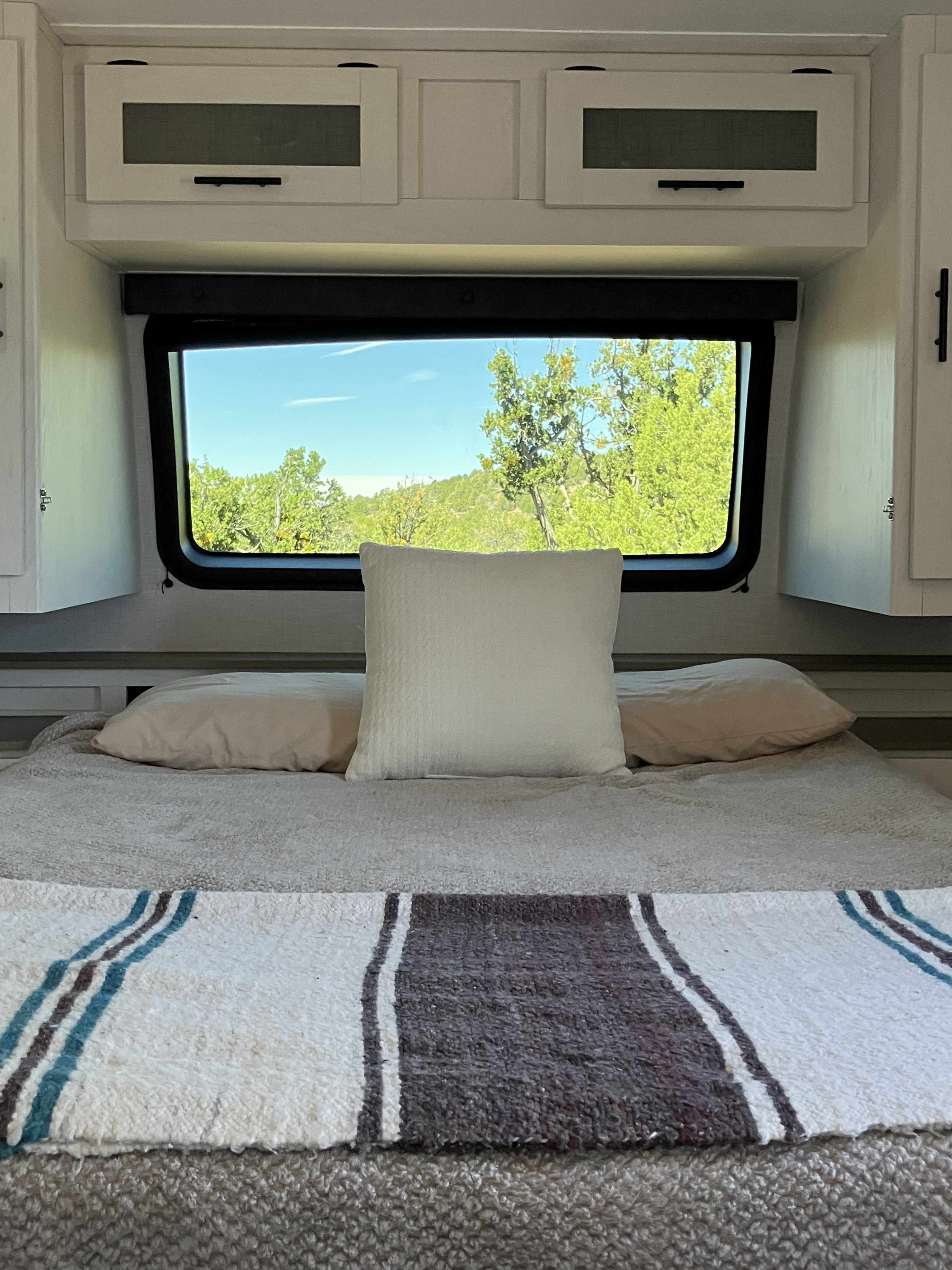 Cozy RV rental bedroom with a nature view through the window, featuring a bed, pillows, and white cabinets.. Forest River Coleman Rubicon 2023