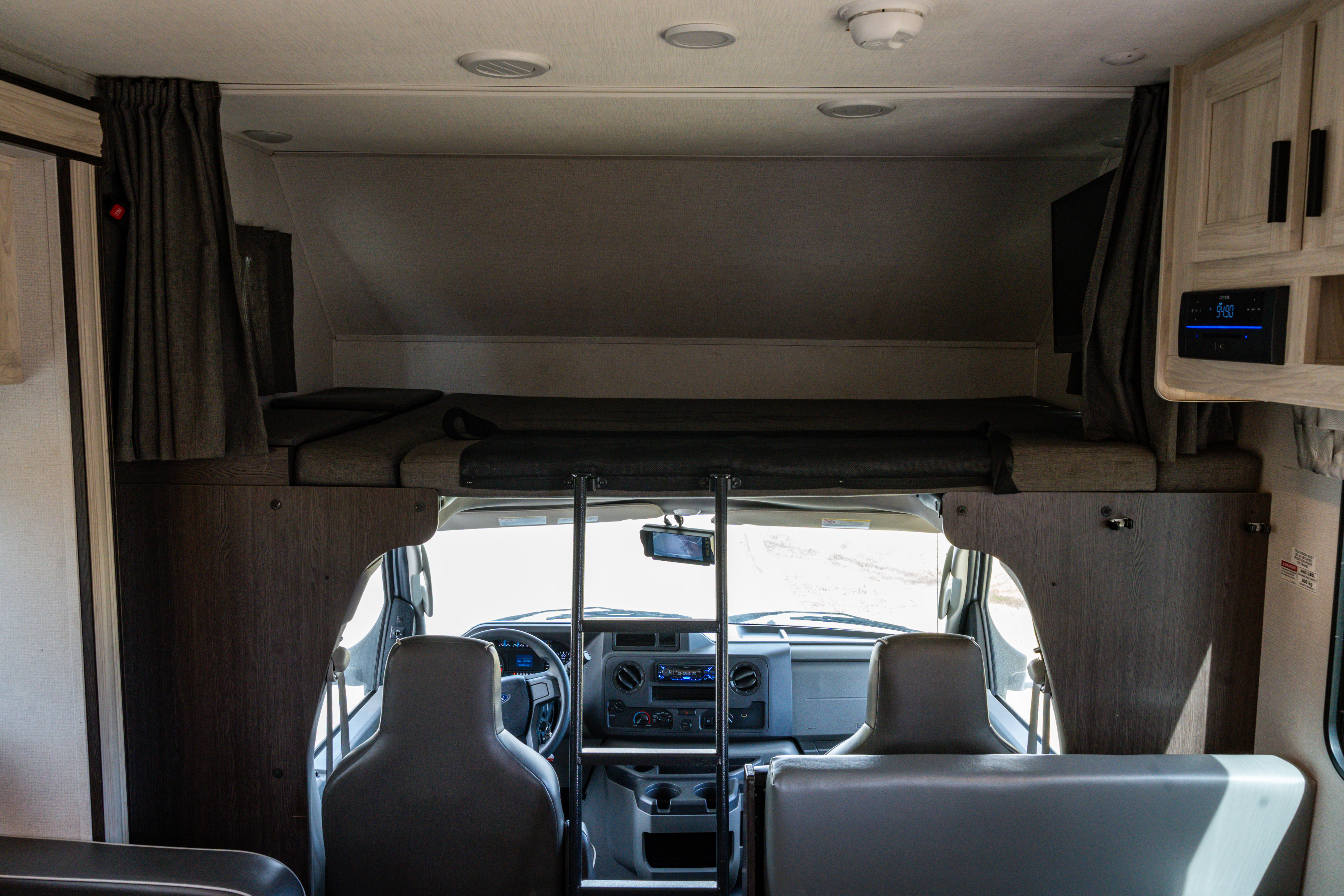 Inside this rv rental, view towards the front cab with an overhead bunk, ladder, and media console. Comfort for your journey!. Forest River Sunseeker LE 2022