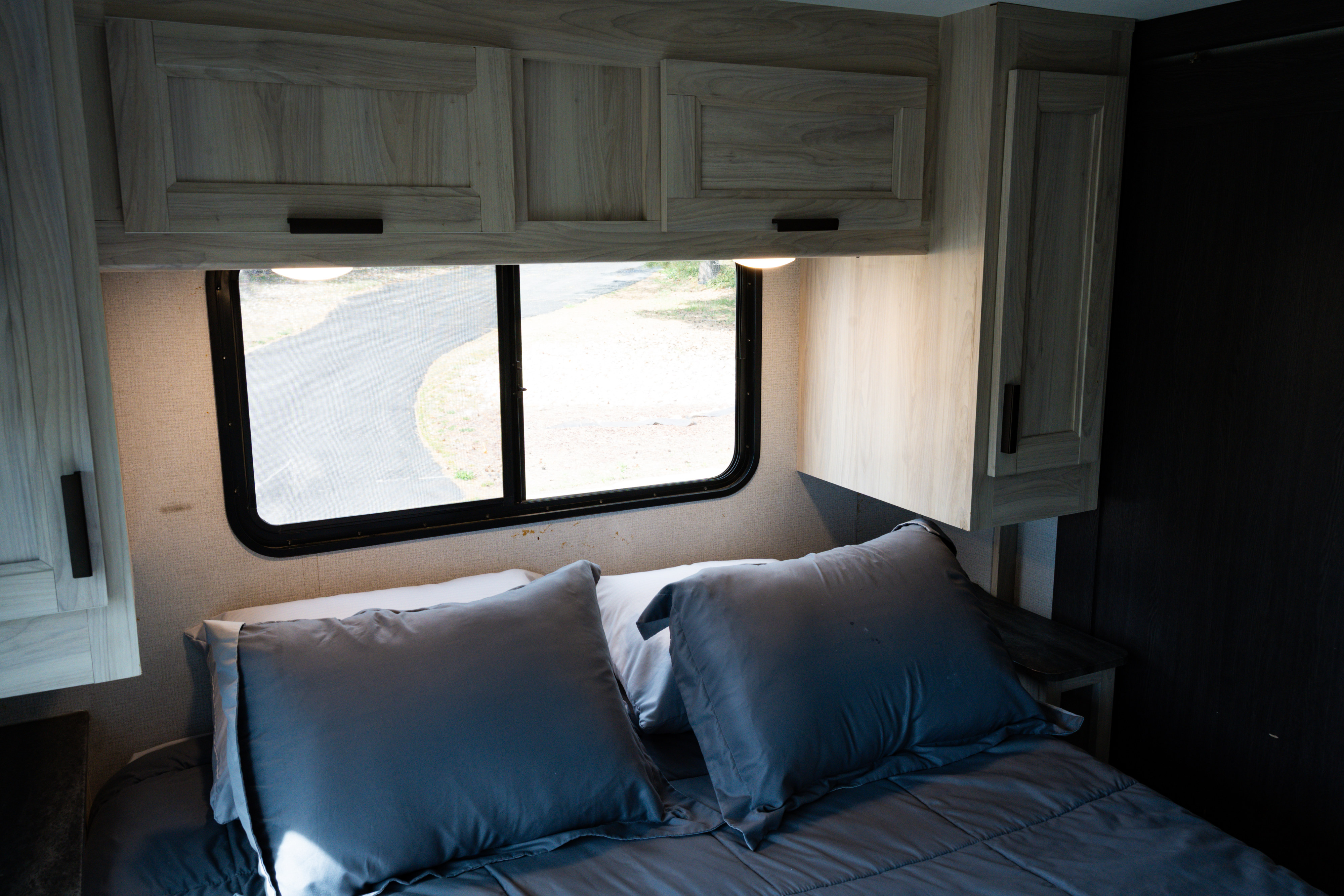 Experience comfort in this RV rental bedroom: light wood cabinets, cozy bed with grey bedding, and a window view.. Forest River Sunseeker LE 2022