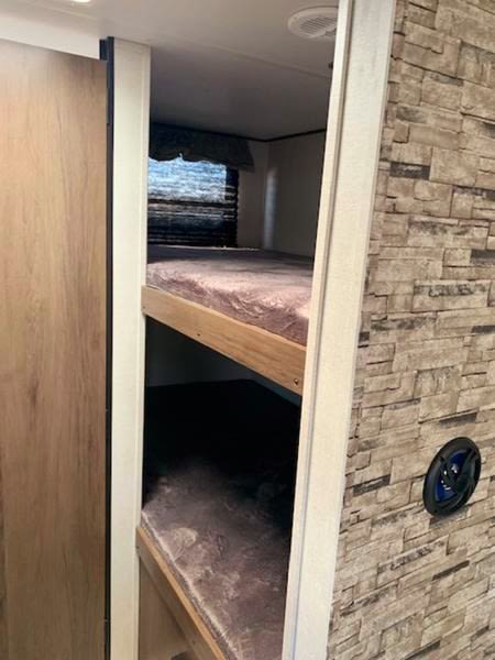 Interior of an rv rental showing bunk beds, a window with blinds, and a speaker on a stone-look wall.. Avenger 26BBS 2021