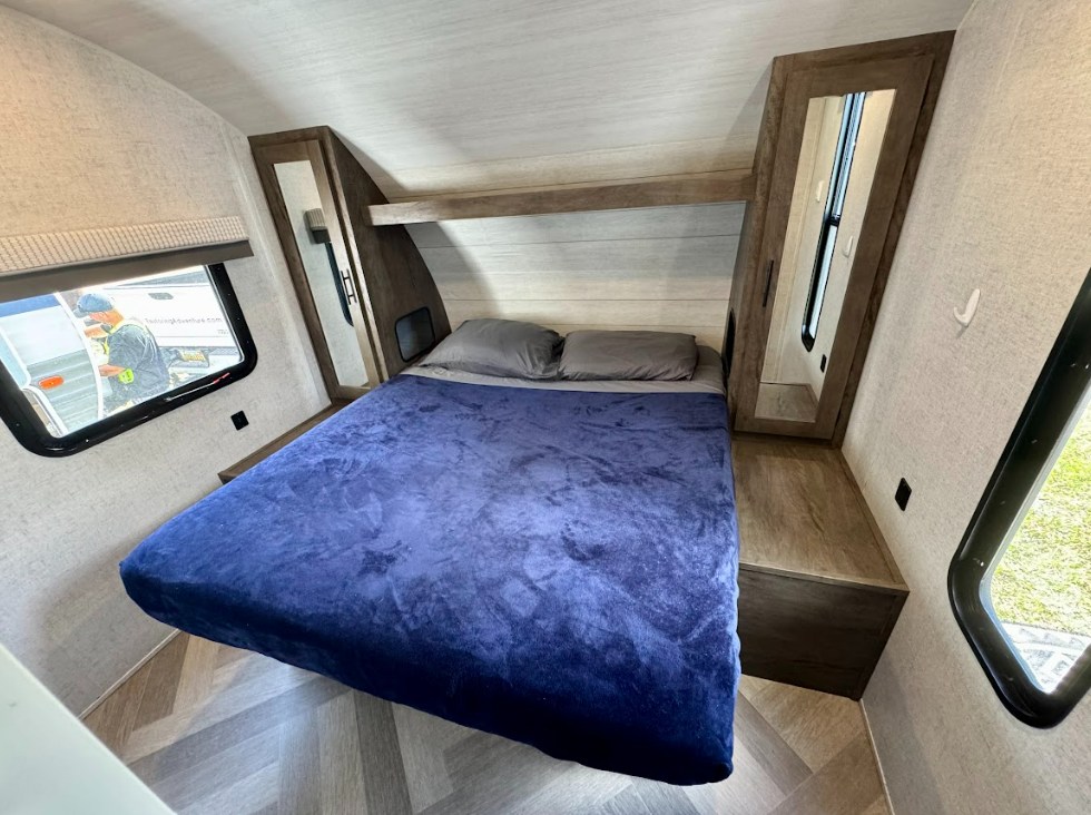 Modern RV rental bedroom with a blue-blanketed bed, built-in storage, and windows. Ready for comfortable travel adventures.. Wildwood 263BHXL 2021