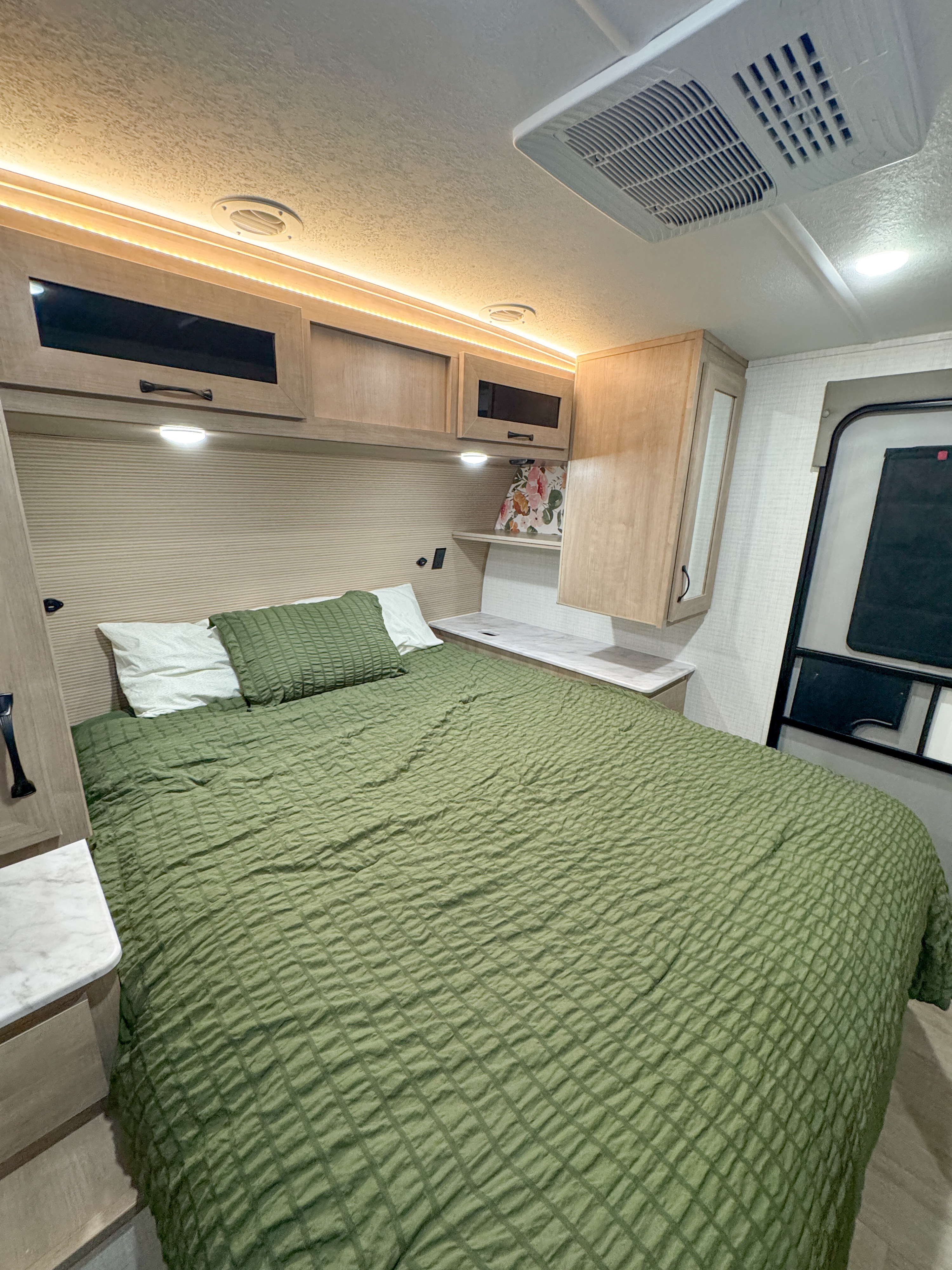 Experience comfortable travel in this RV rental bedroom, featuring green quilted bedding, ample storage, and ceiling AC. A cozy retreat.. Forest River Palomino Solaire 2025
