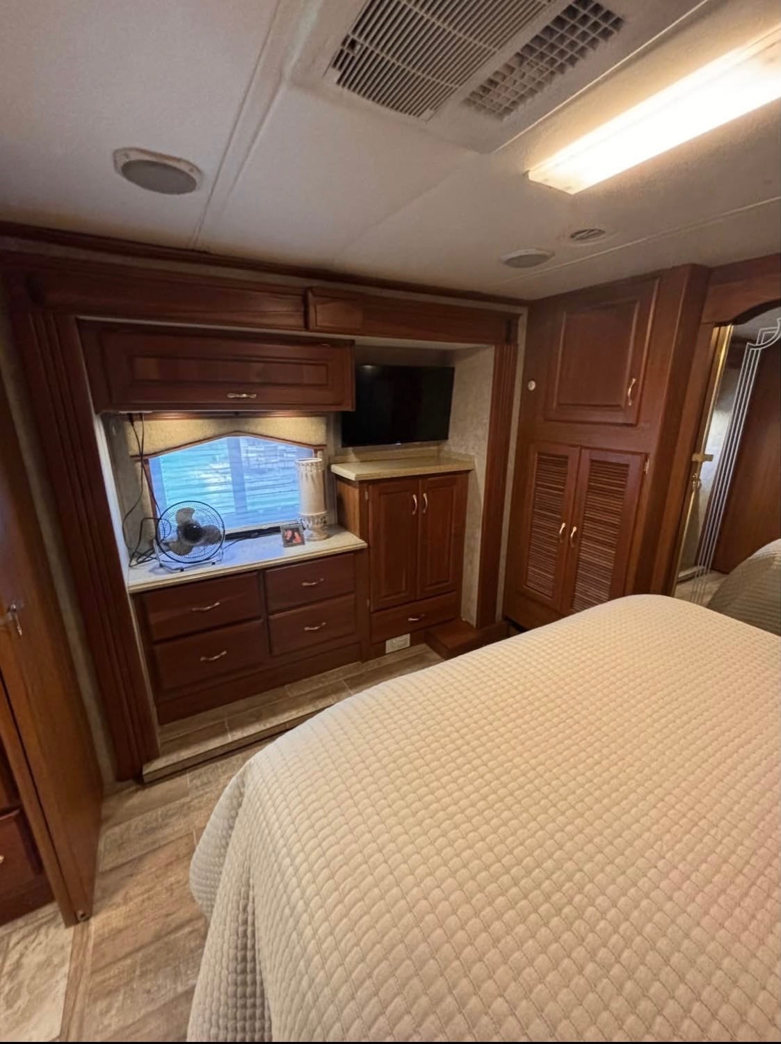 Spacious RV rental bedroom. Features dark wood cabinetry, a comfortable quilted bed, window, fan, and TV.. Beaver Santiam 2005