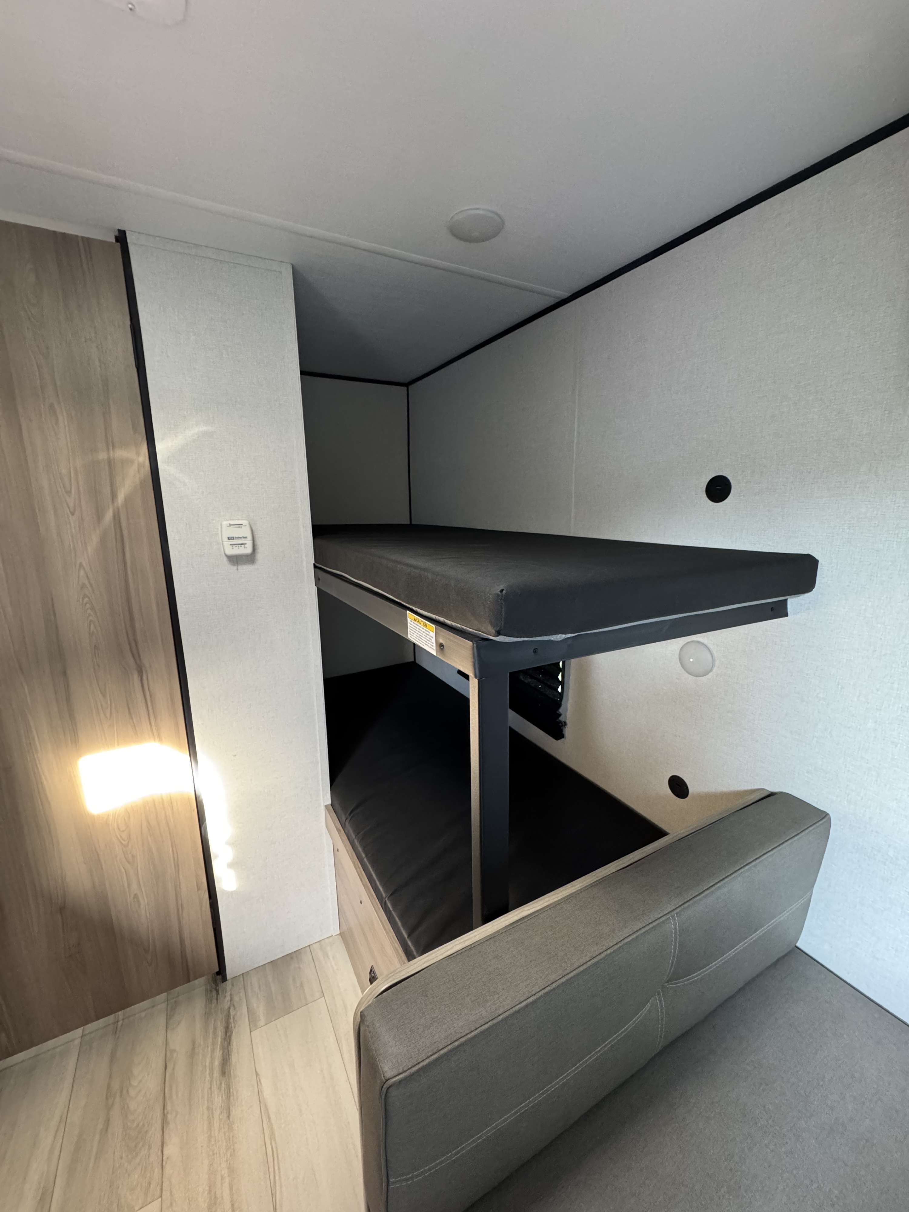 RV rental interior with practical bunk beds, a cushioned lower seat, and a thermostat on the wall. Compact living space.. Dutchmen Coleman 2025
