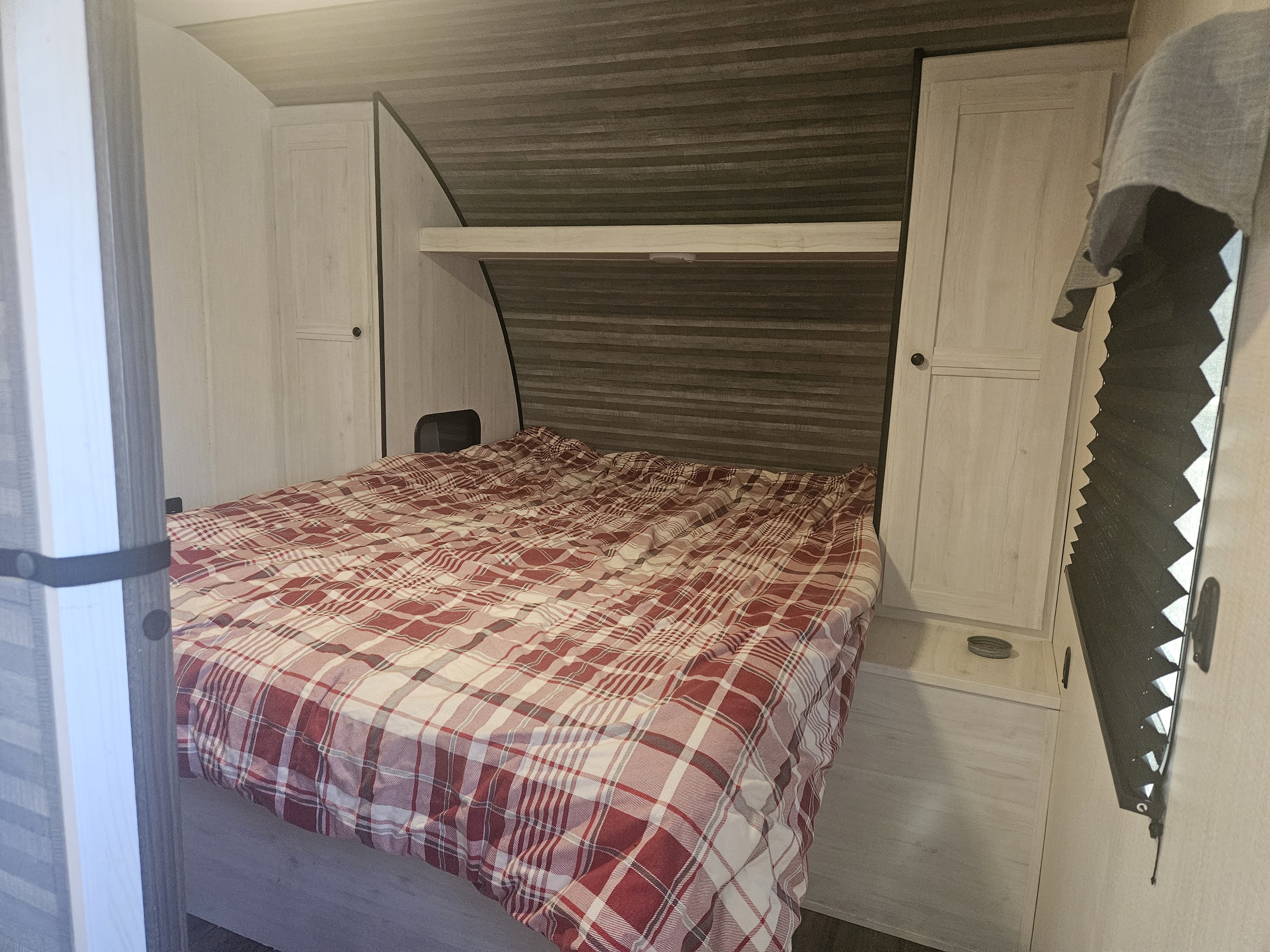 RV rental bedroom with a comfy plaid bed, built-in side cabinets, an overhead shelf, and pleated window shade.. Heartland RVs Trail Runner 2024