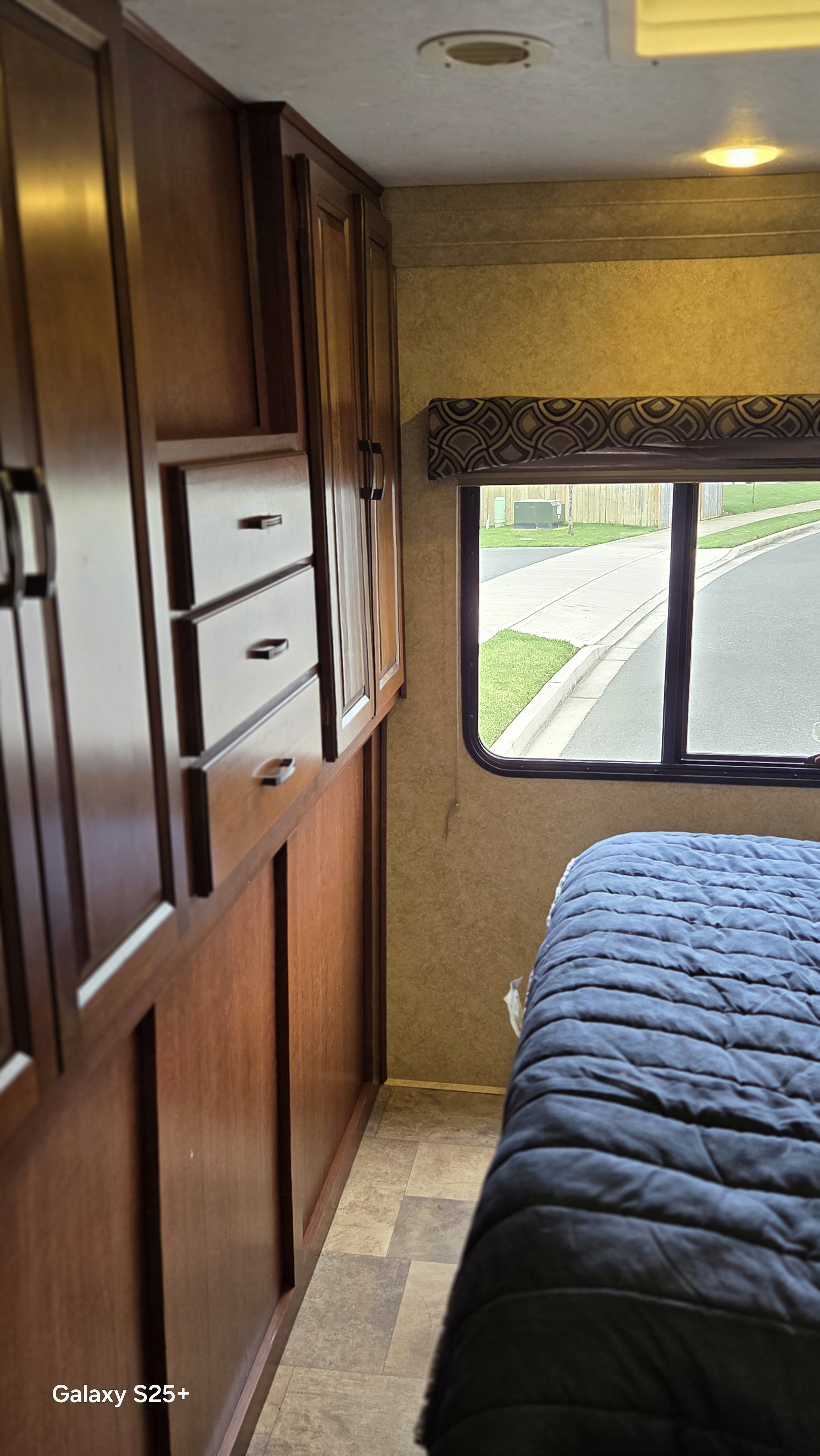 RV rental bedroom: wooden cabinets, drawers, and a cozy bed with a window view of the street outside.. Forest River Sunseeker 2014