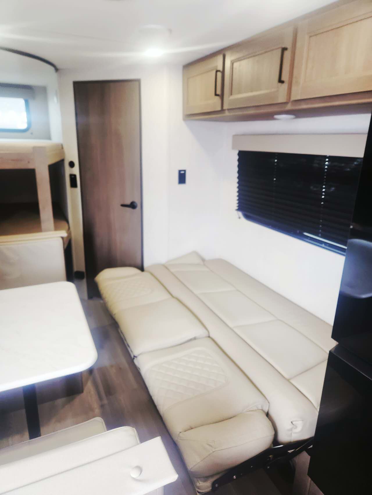 RV rental interior: a modern living space featuring a sofa bed, bunk beds, dining table, and overhead cabinets.. Grand Design Transcend Xplor 2025