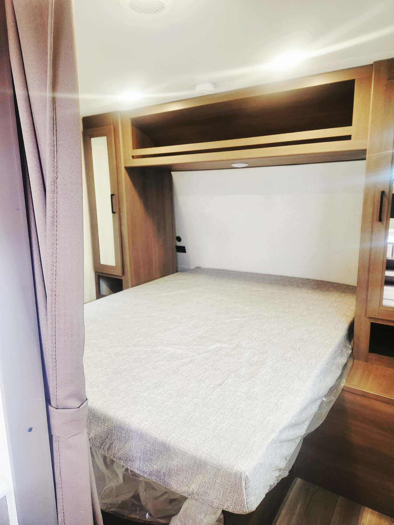 RV rental bedroom with bed, overhead wooden cabinets, and side wardrobes. A cozy, compact sleeping area for your travels.. Grand Design Transcend Xplor 2025