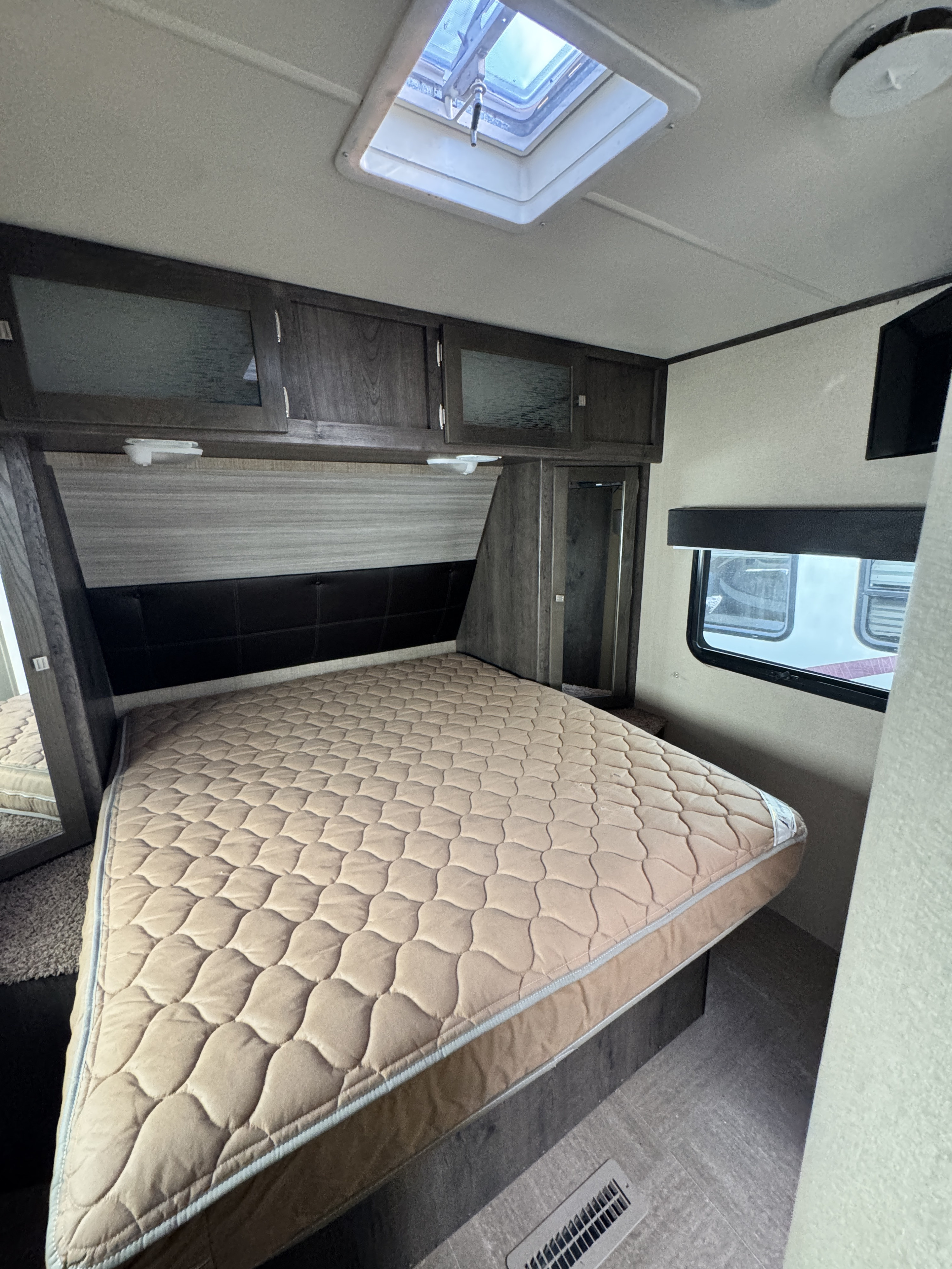 RV rental bedroom with a comfortable quilted bed, overhead cabinets, window, and skylight for cozy travel.. Dutchmen Kodiak 2015