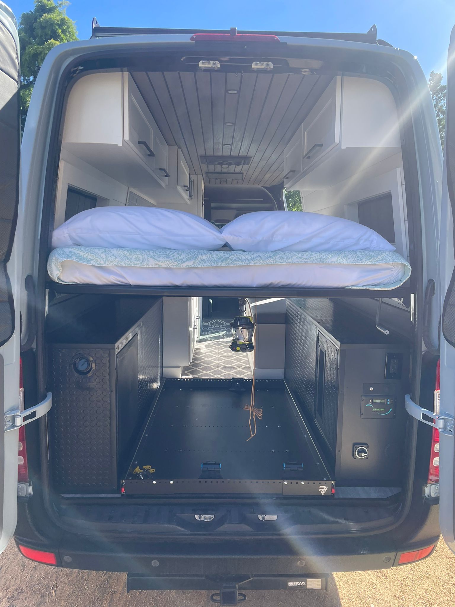 Inside a modern rv rental camper van, featuring an elevated bed, pull-out cargo tray, custom cabinets, and essential controls.. Mercedes-Benz Sprinter RV Motorhome Campervan 2012