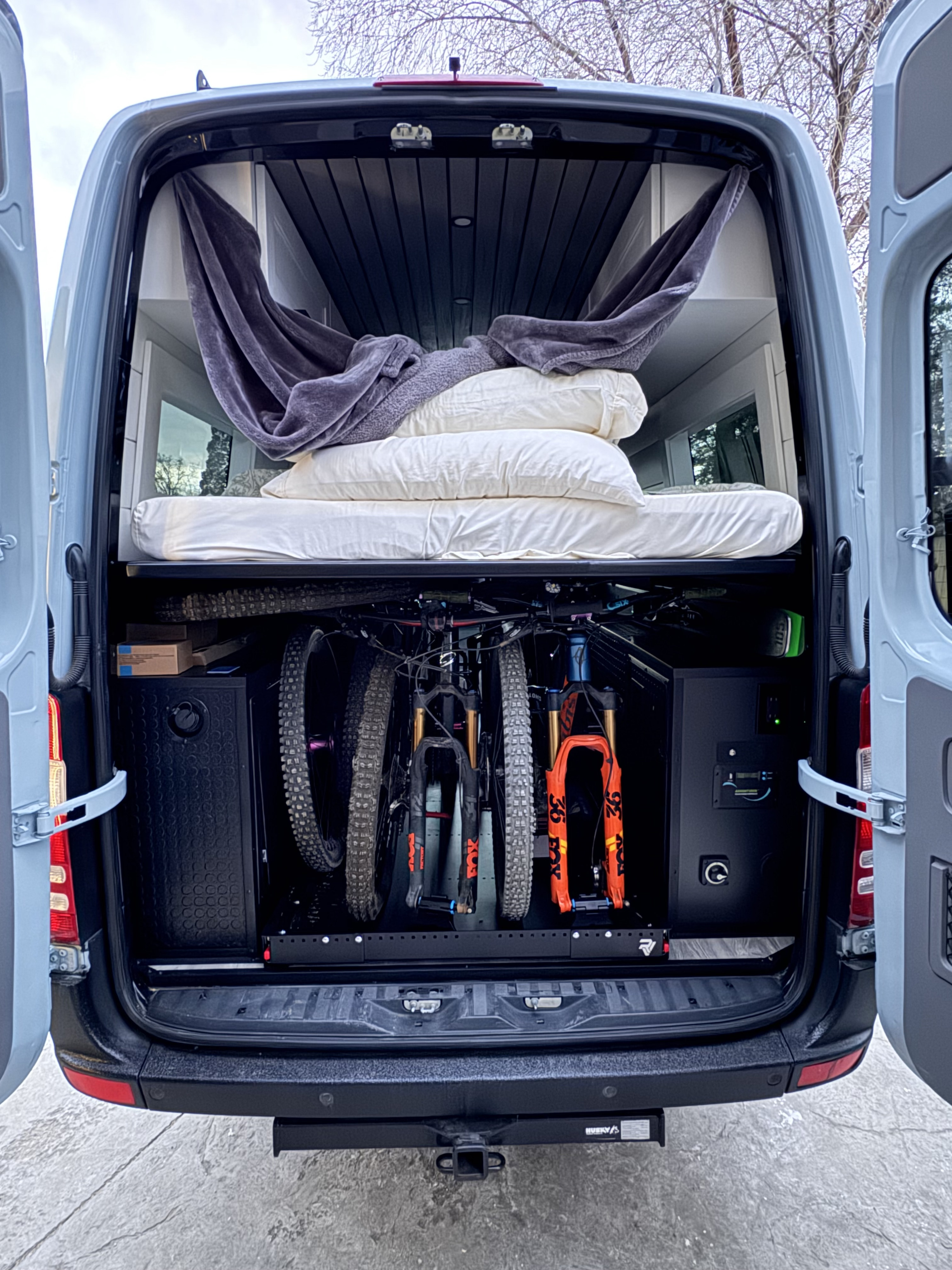 This adventure-ready rv rental shows a bed, hammock, and two mountain bikes stored in the lower garage of a grey camper van.. Mercedes-Benz Sprinter RV Motorhome Campervan 2012