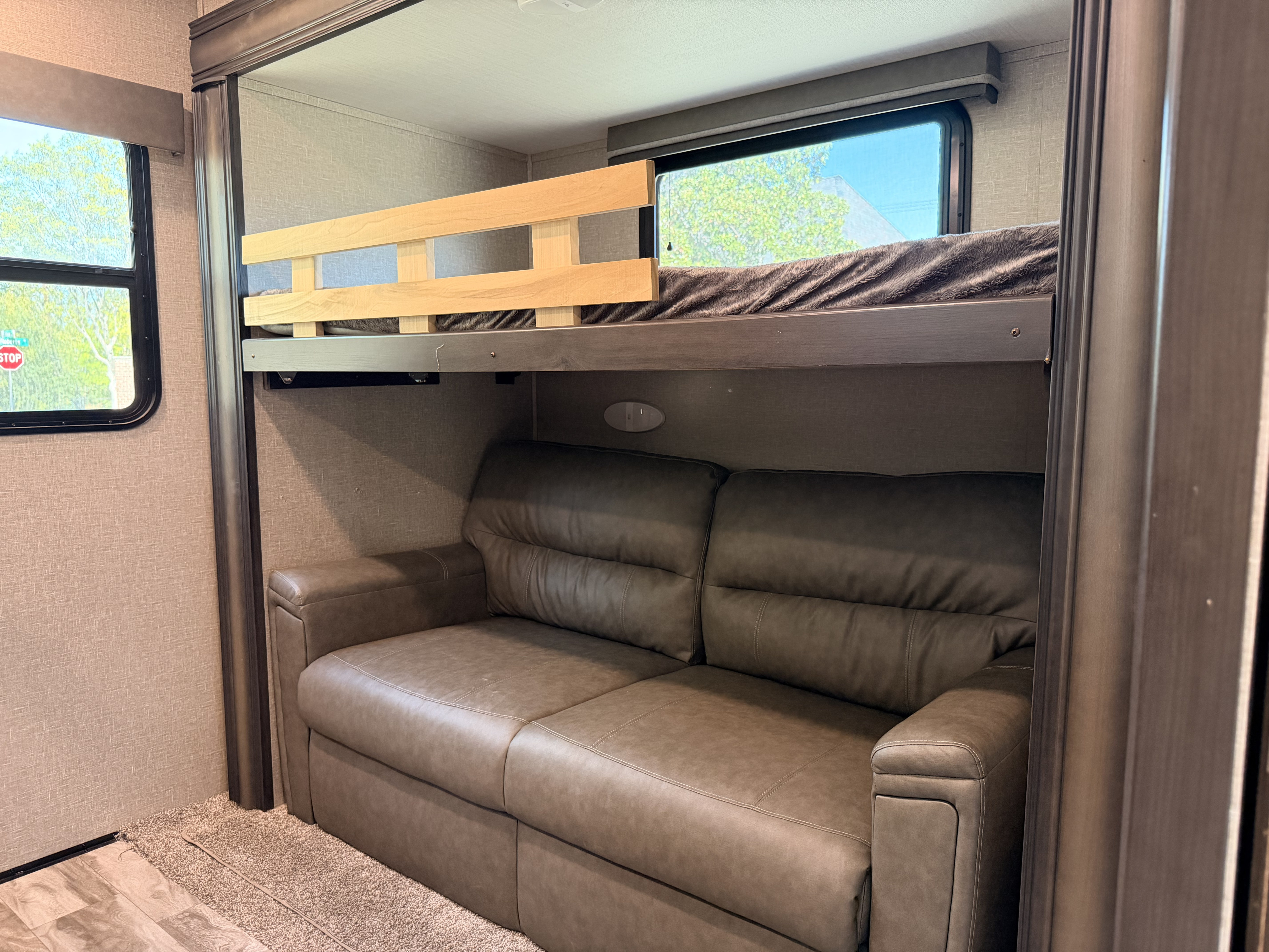 This RV rental's interior features bunk beds above a brown sofa, with windows showing outdoor scenery, offering cozy space.. Grand Design Reflection 2022