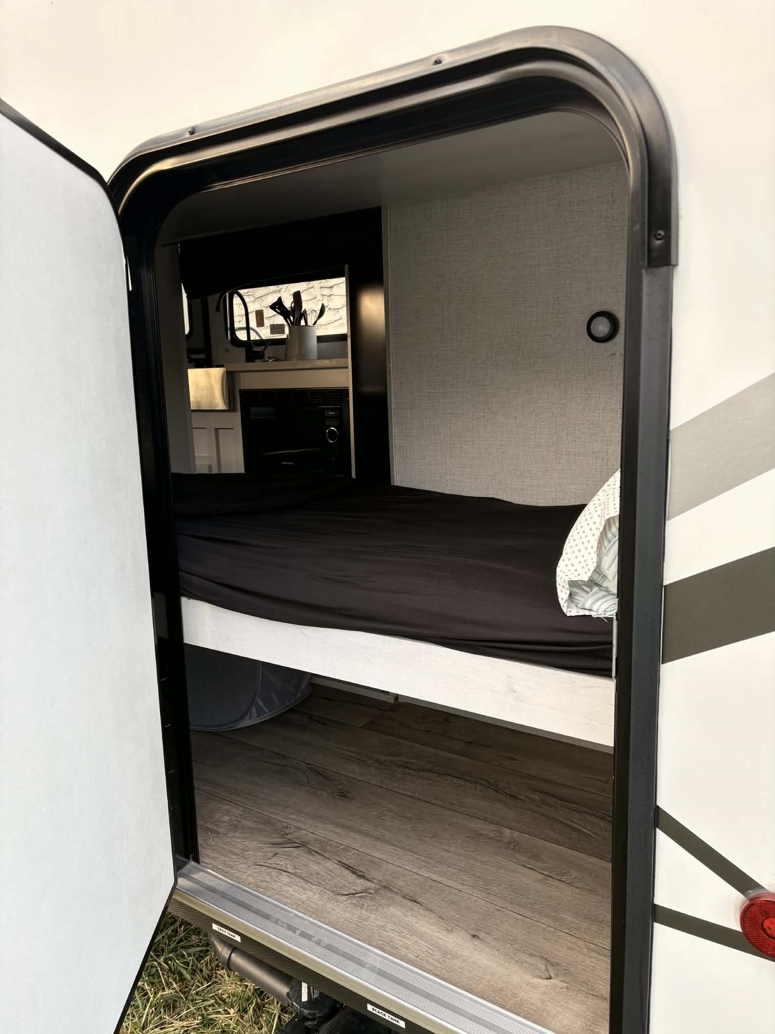 View into a compact rv rental through an open door, showing modern bunk beds, wood-look floor, and a small kitchen.. Dutchmen Coleman Rubicon 2021