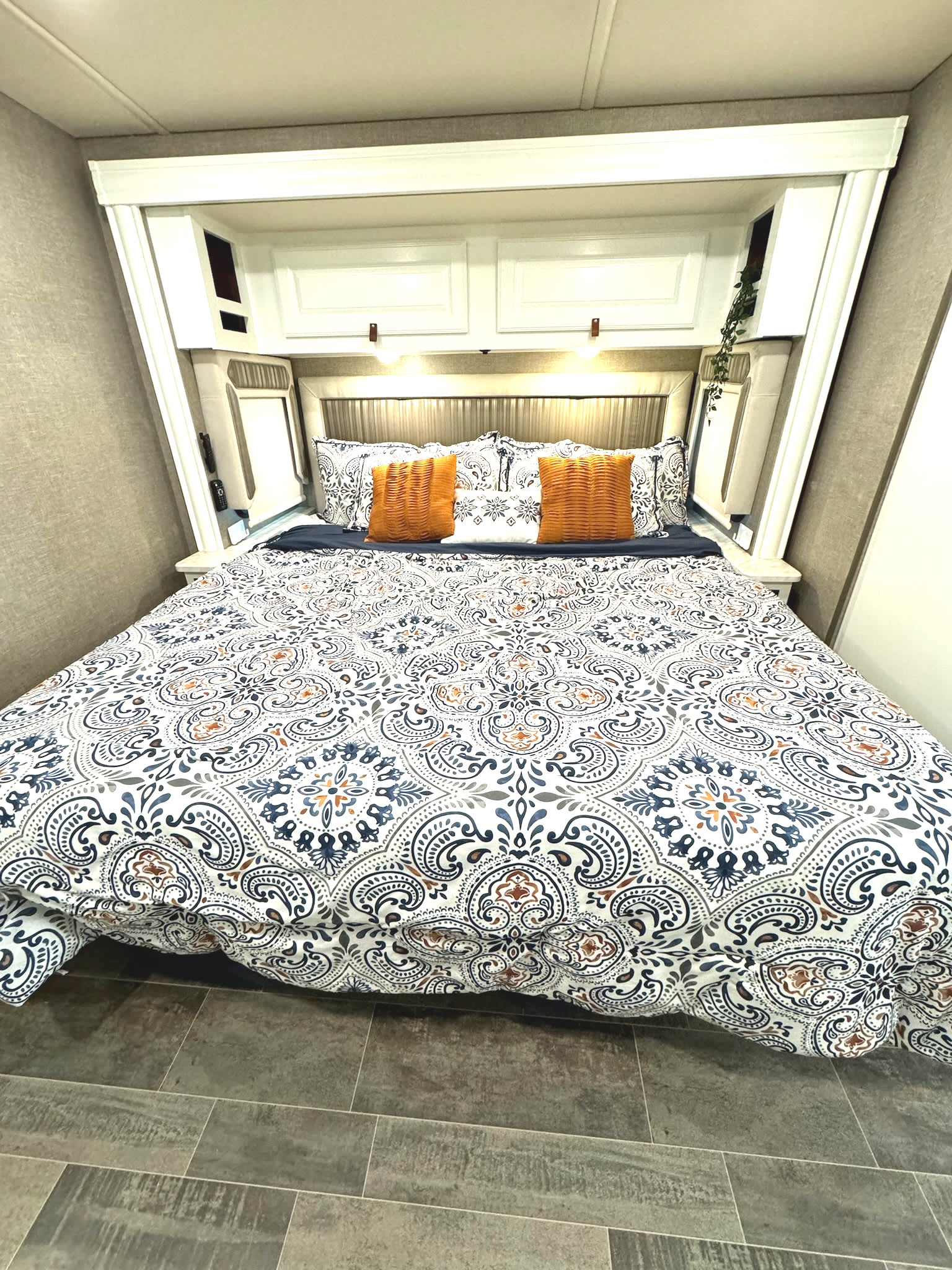 Cozy RV rental bedroom with a detailed patterned duvet, bright orange pillows, and clever overhead storage.. Winnebago Adventurer 2020
