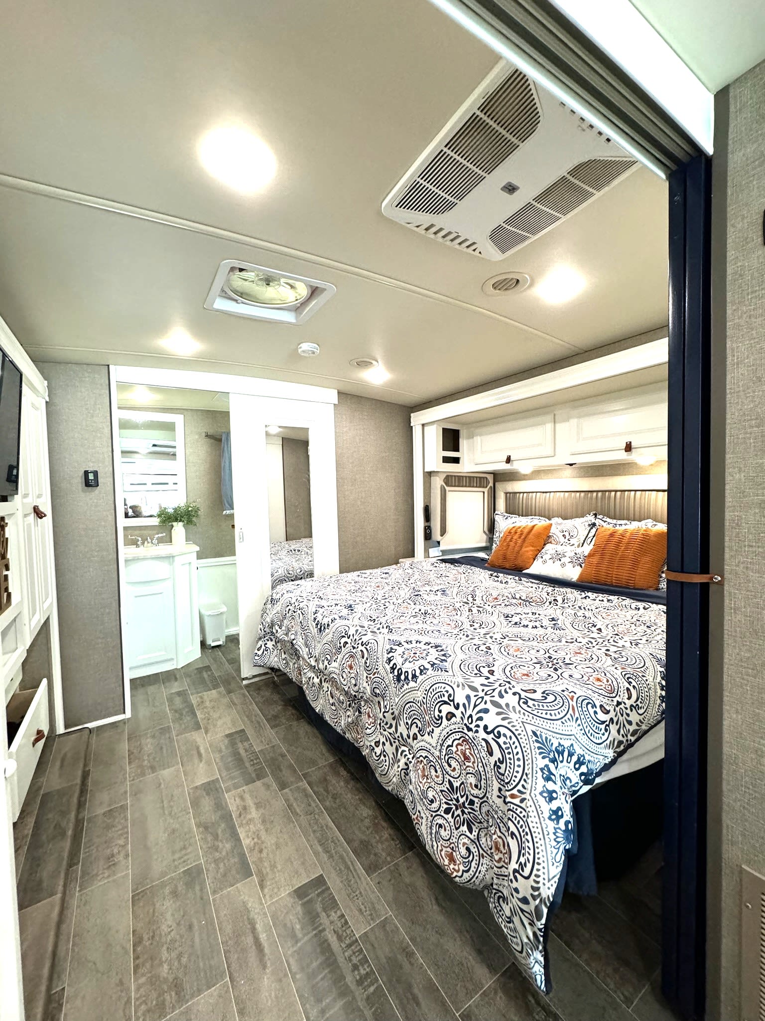 Cozy RV rental bedroom with a patterned comforter, orange pillows, vanity area, and overhead storage for a comfortable stay.. Winnebago Adventurer 2020