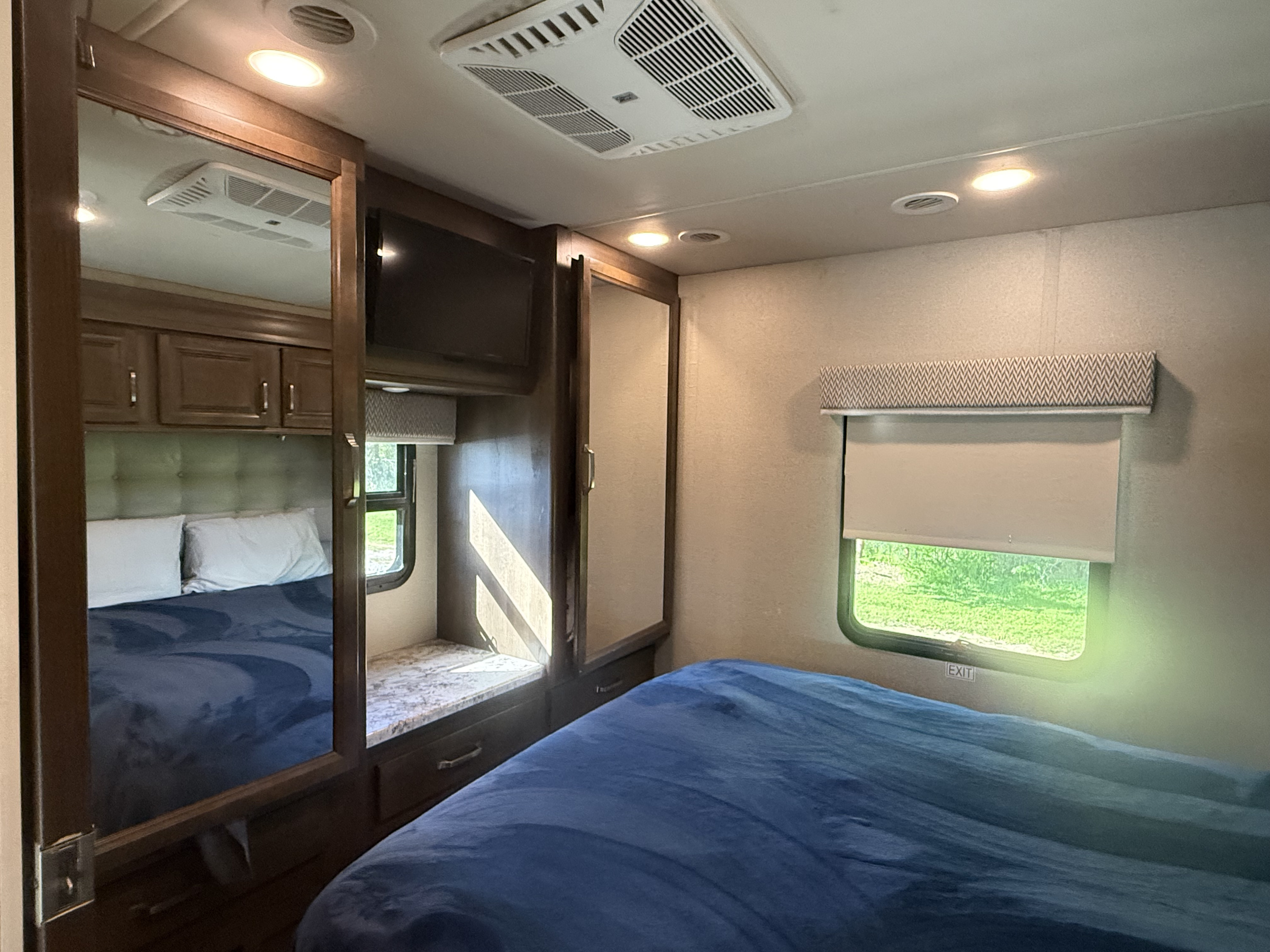 Bright RV rental bedroom with a large bed, overhead cabinets, TV, and window. Ideal for comfortable travel.. Entegra Coach Esteem 2020