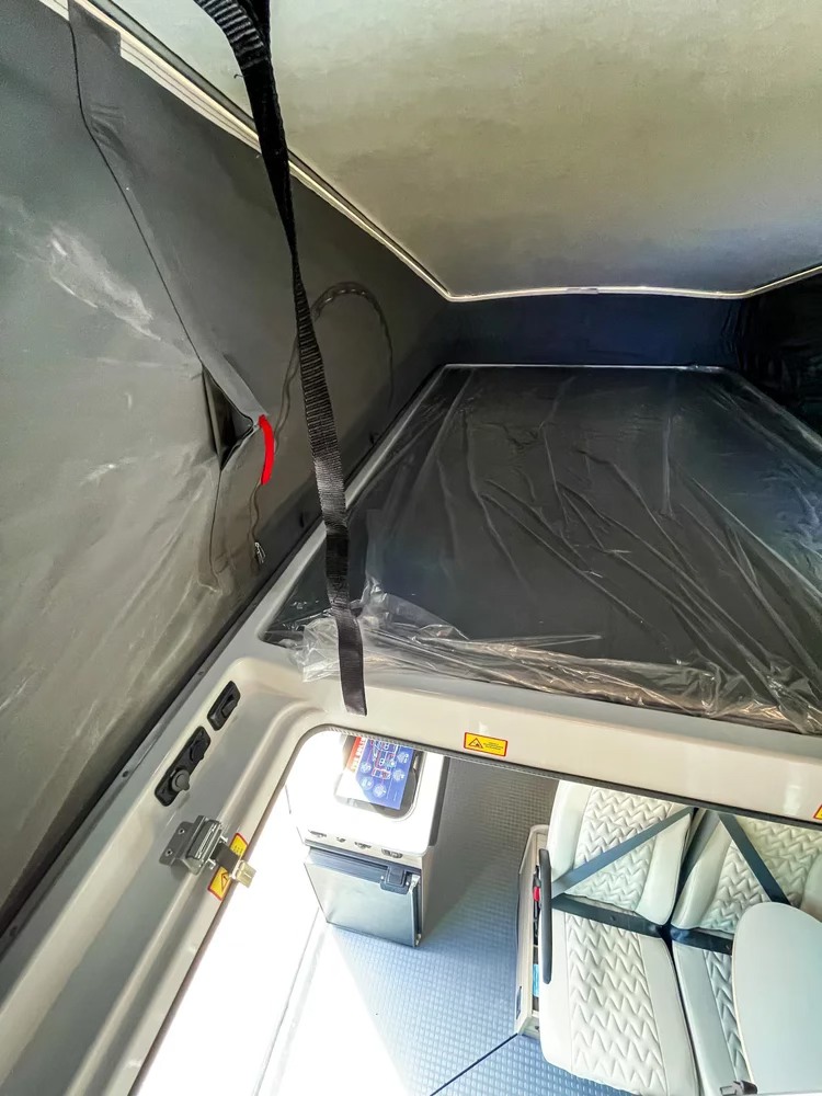 Inside an RV rental: pop-top bed with plastic covering, compact kitchen with fridge, and textured rear seats.. Winnebago Solis 2022