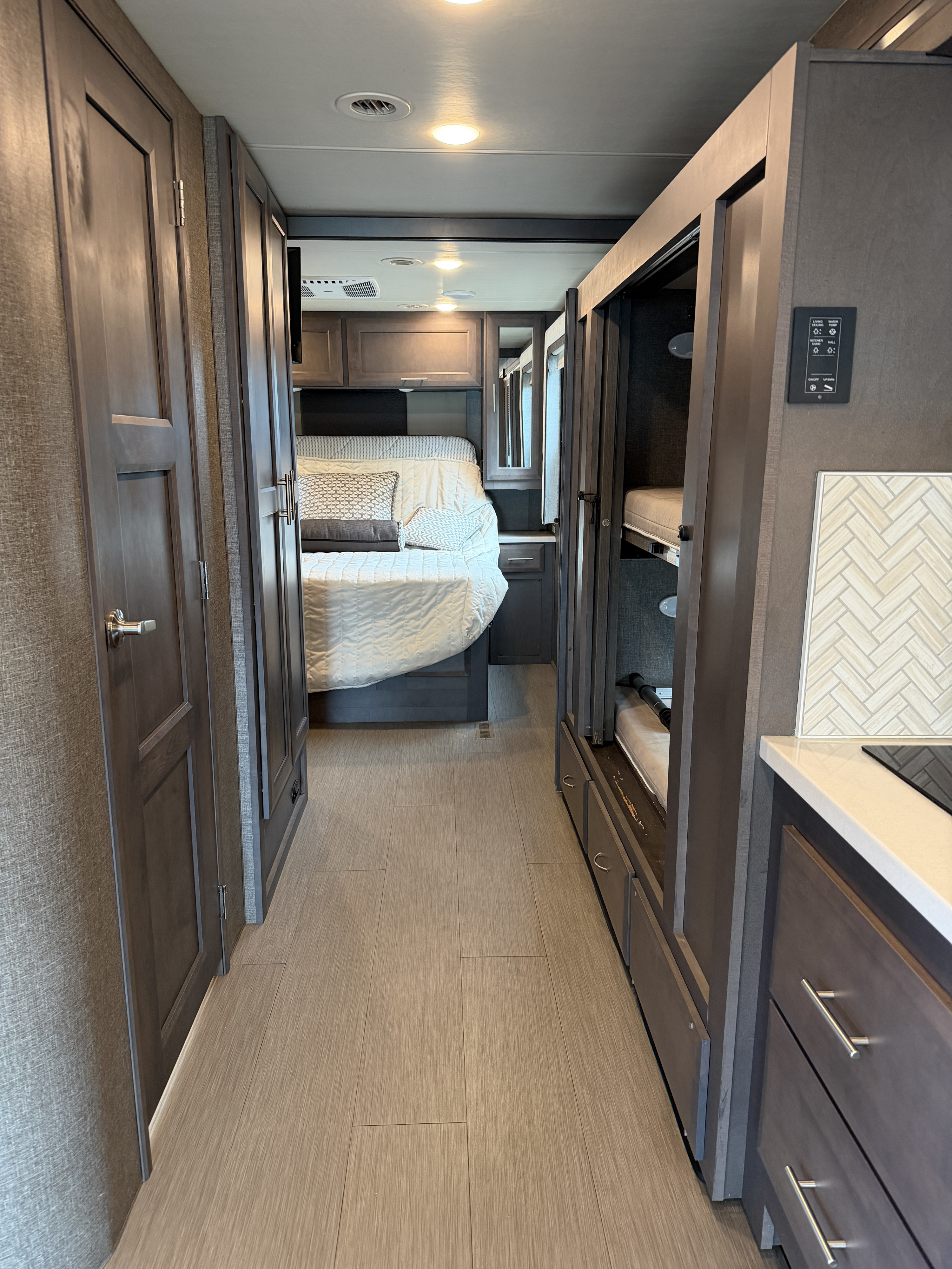 Modern rv rental interior with a hallway leading to a bedroom, bunk beds on the right, and a kitchen counter.. Thor Palazzo 2022