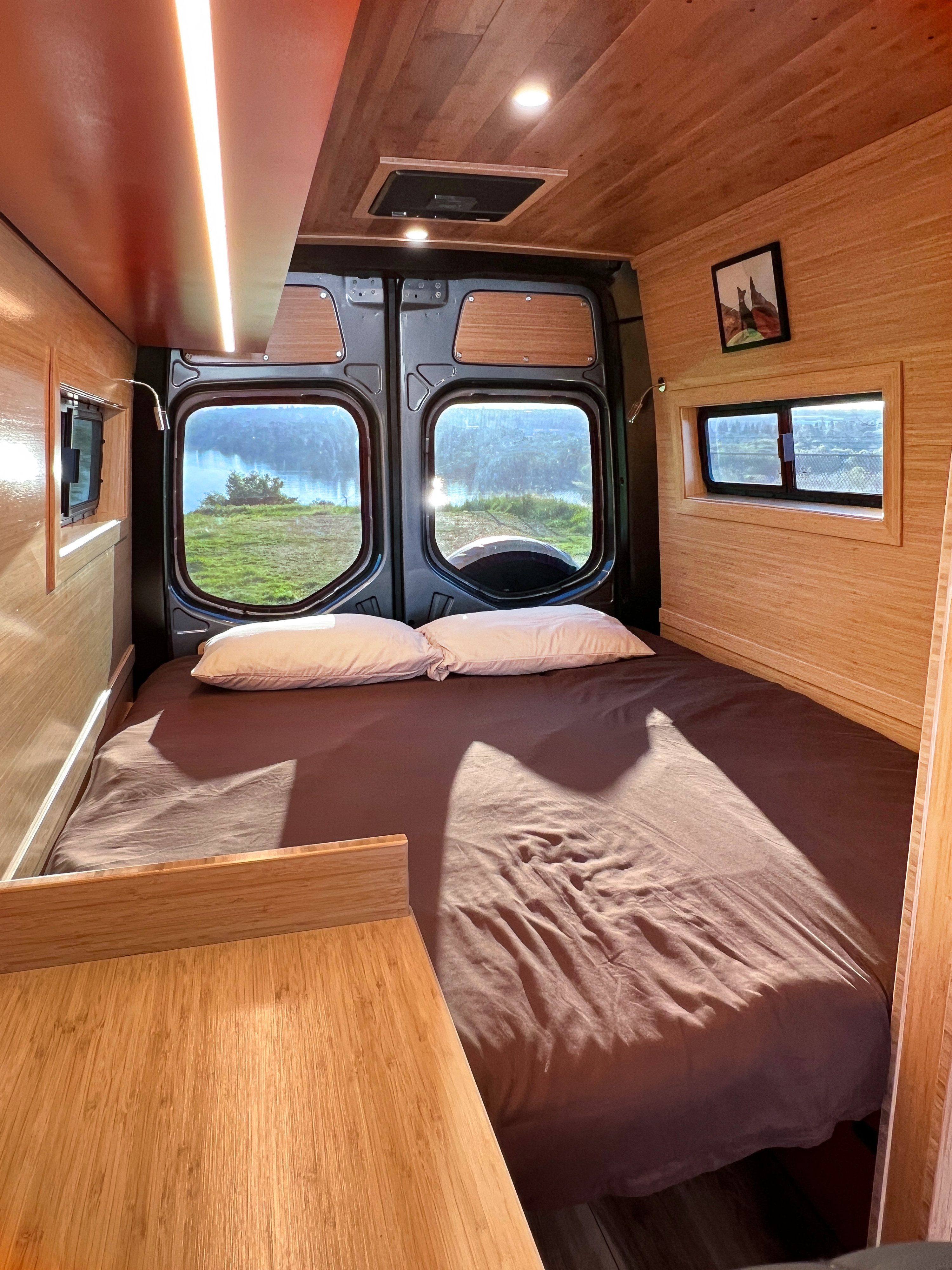 Relaxing RV rental bedroom with a large bed, warm wood interior, and stunning lake views out the back windows.. Mercedes-Benz Sprinter 2025