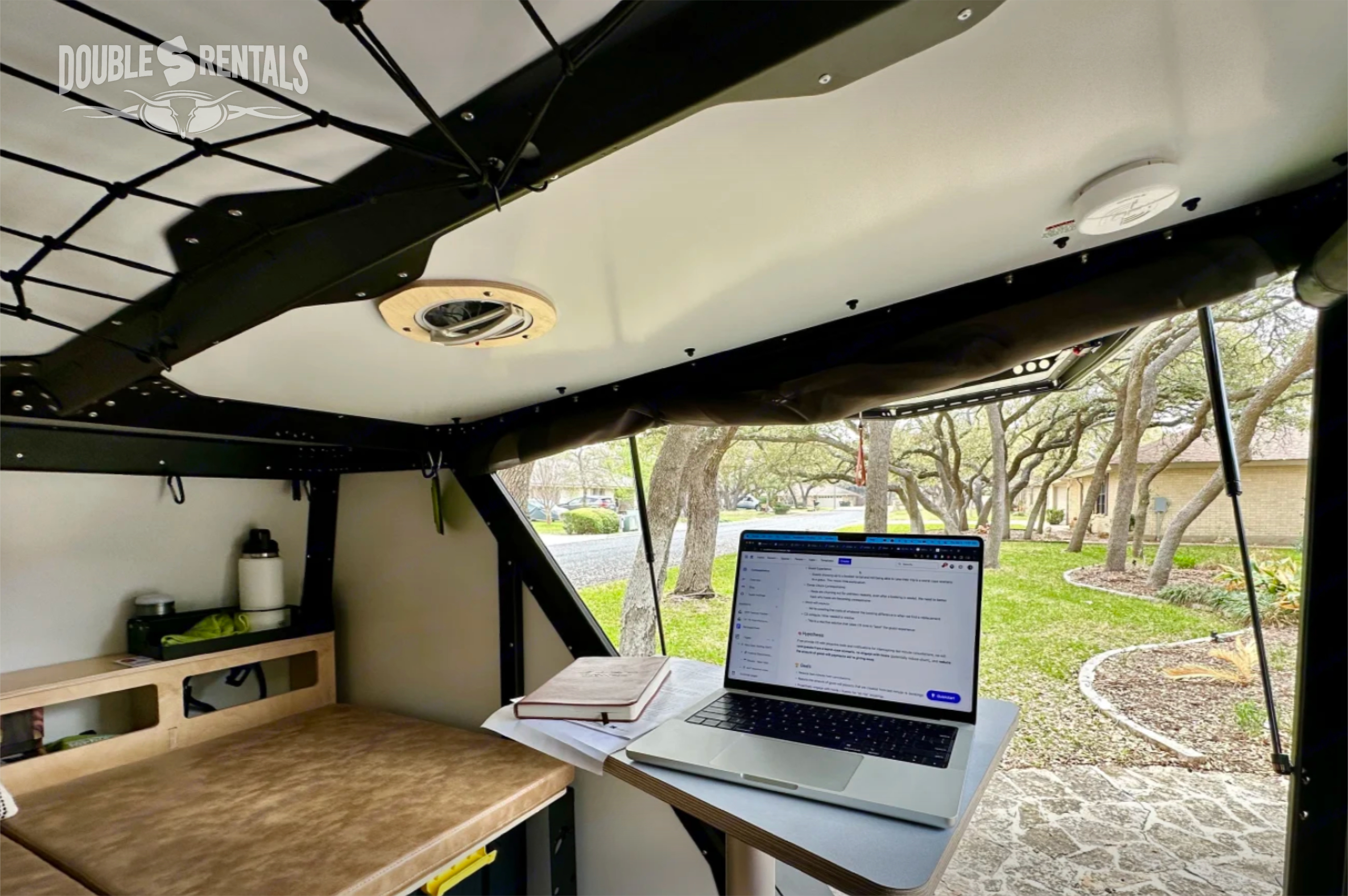 Double S RV rental offers a mobile office setup: laptop, bed, and a green outdoor view from the camper.. TAXA TigerMoth 2023