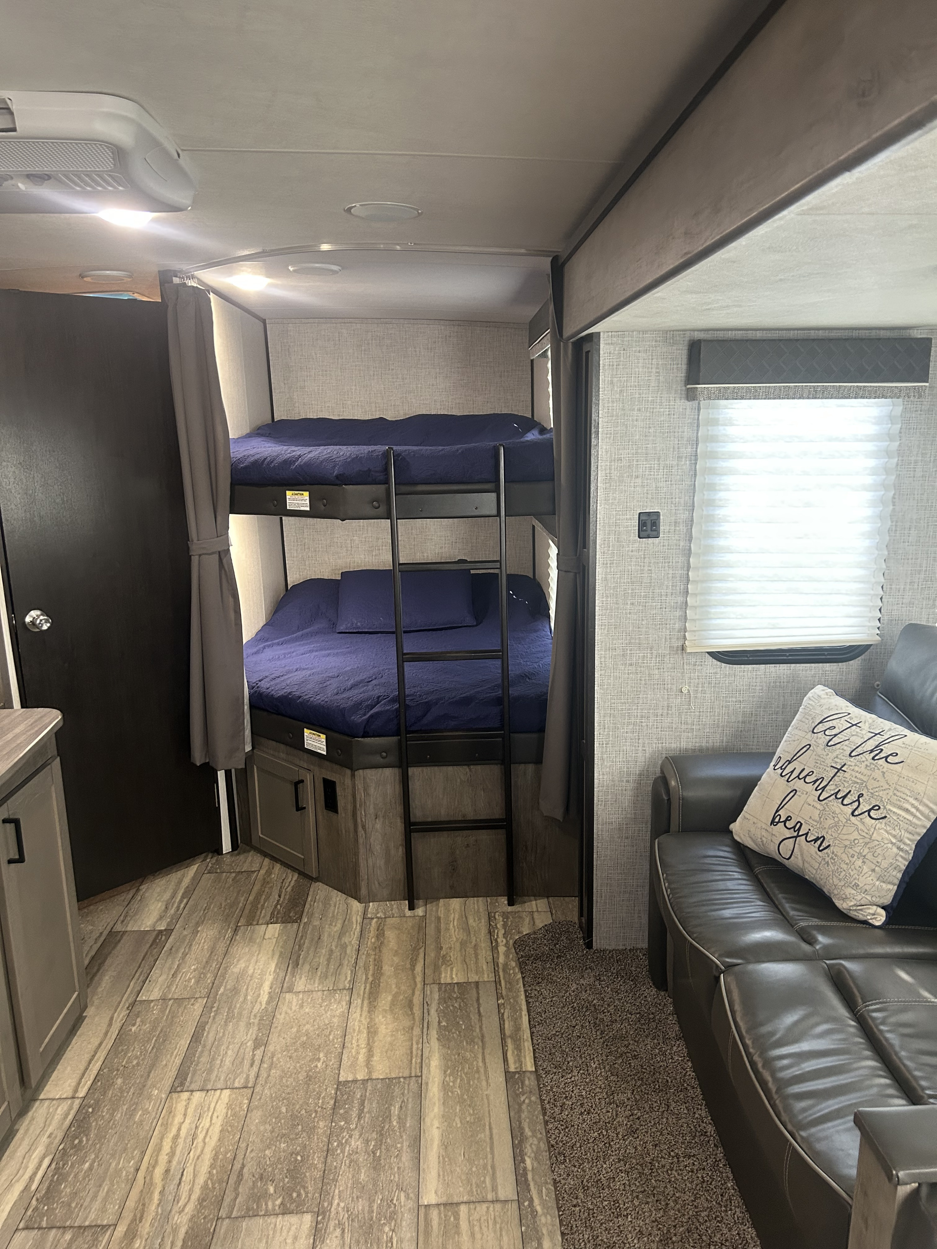 RV rental interior: cozy bunk beds with blue bedding, a comfy sofa with a pillow, and wood-look flooring and carpet.. Heartland RVs North Trail 2020