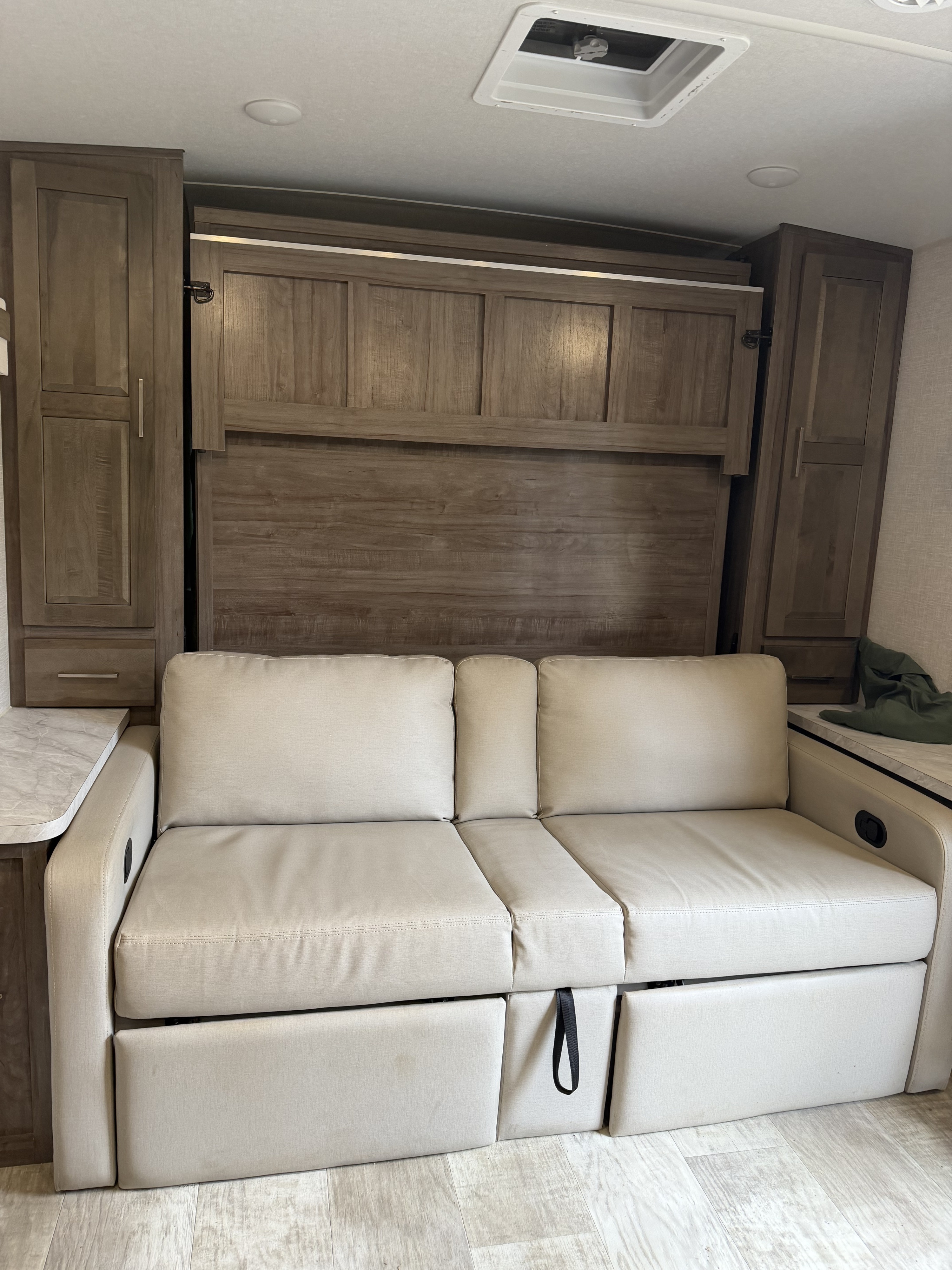 RV rental interior featuring a versatile pull-out sofa and folded murphy bed, optimizing compact living space, flanked by wood cabinetry.. Forest River Rockwood Mini Lite 2023