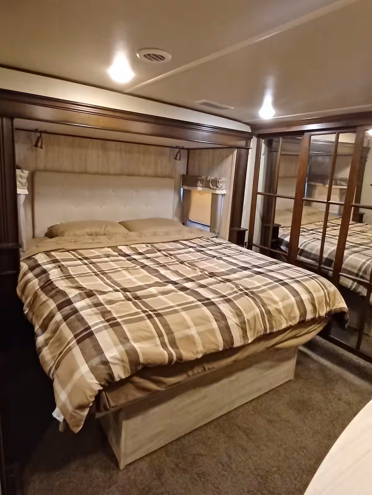 This comfortable RV rental bedroom features a cozy bed with plaid bedding, mirrored storage, and ceiling lights, perfect for travel.. Forest River Palomino Columbus C-Series 2019