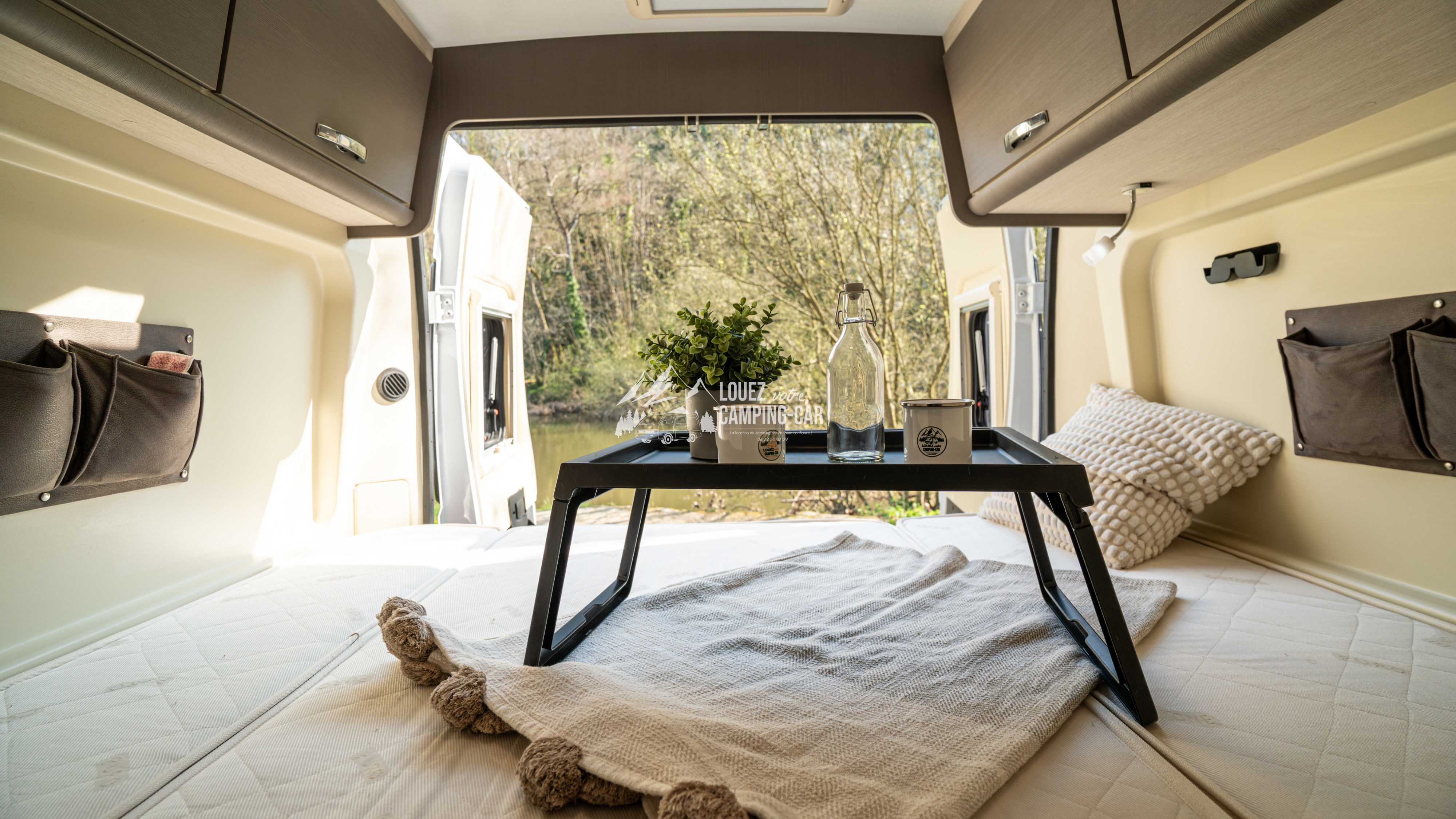 Cozy RV rental interior with a bed, breakfast tray, and a beautiful nature view through the open rear doors.. CHALLENGER V114 2018