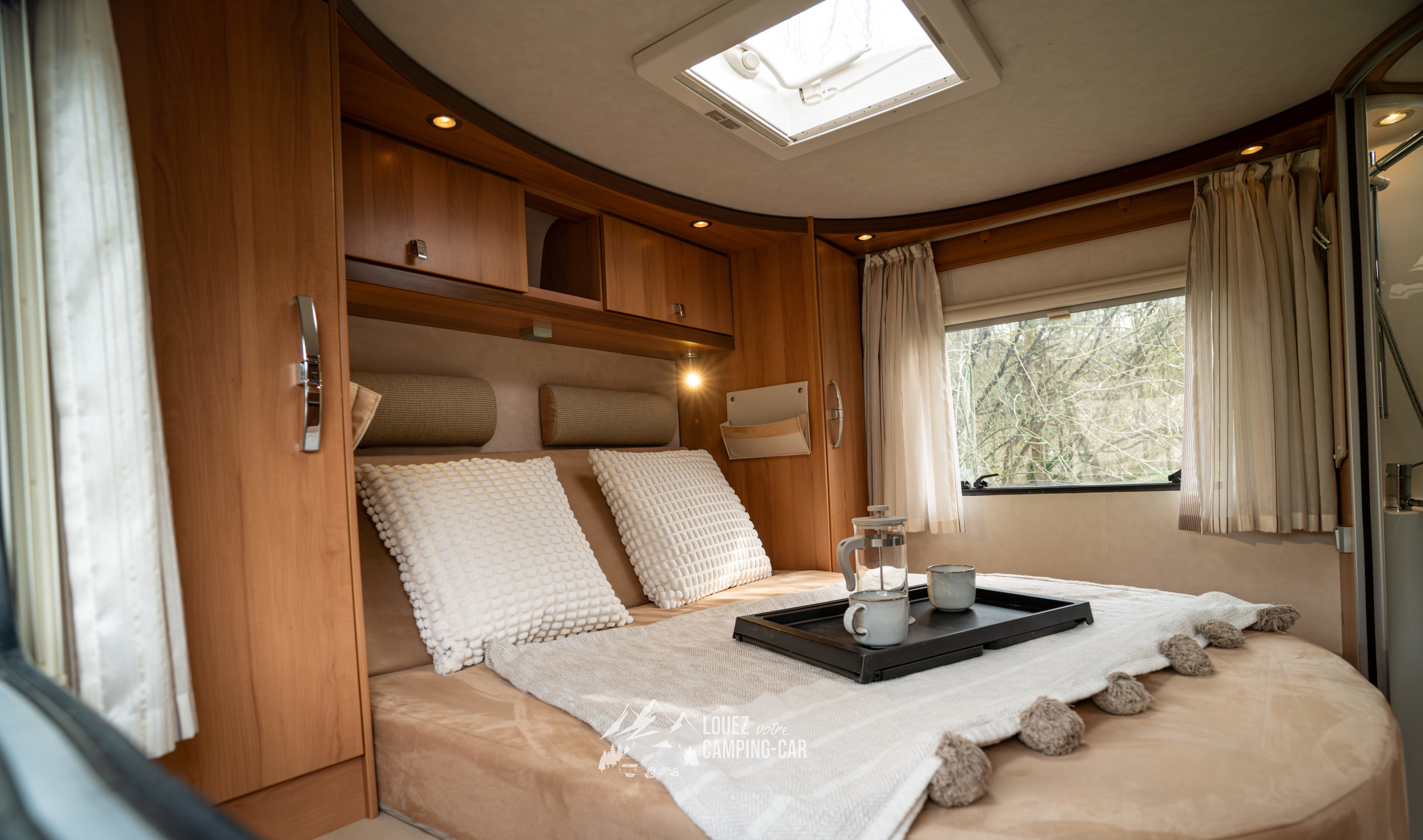 Cozy RV rental bedroom featuring a comfortable bed, skylight, wooden cabinets, and a breakfast tray. Ideal for road trips.. HYMER T698 2012
