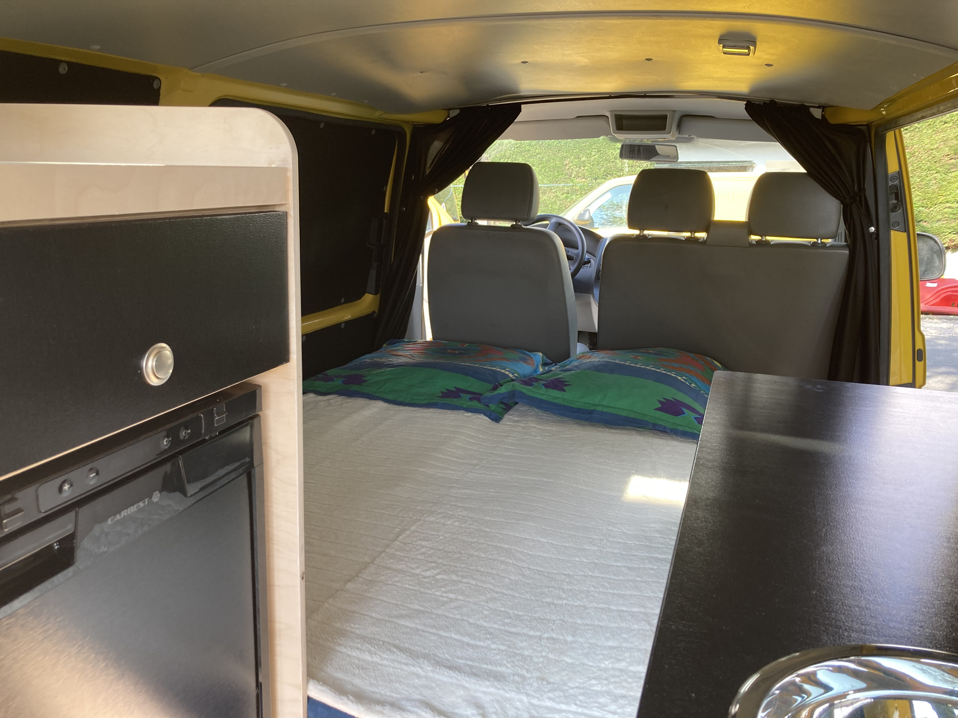 RV rental: Inside a yellow camper van, featuring a comfy bed, a small fridge, and kitchen space.. Volkswagen Transporter 2010