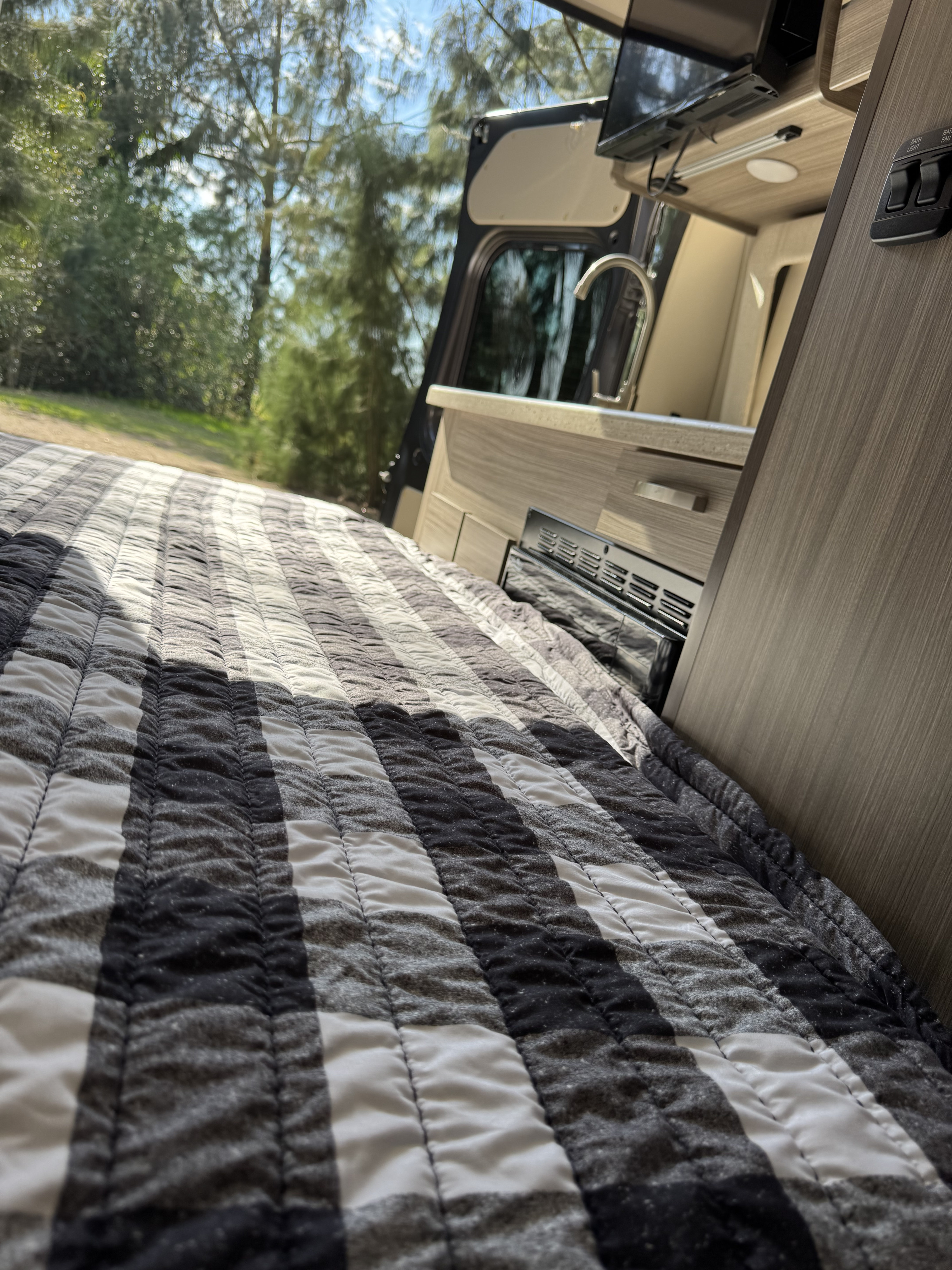 RV rental: inviting bed with black & white striped quilt, mini-kitchen, and serene nature visible through the open door.. Entegra Coach Ethos 20a 2022
