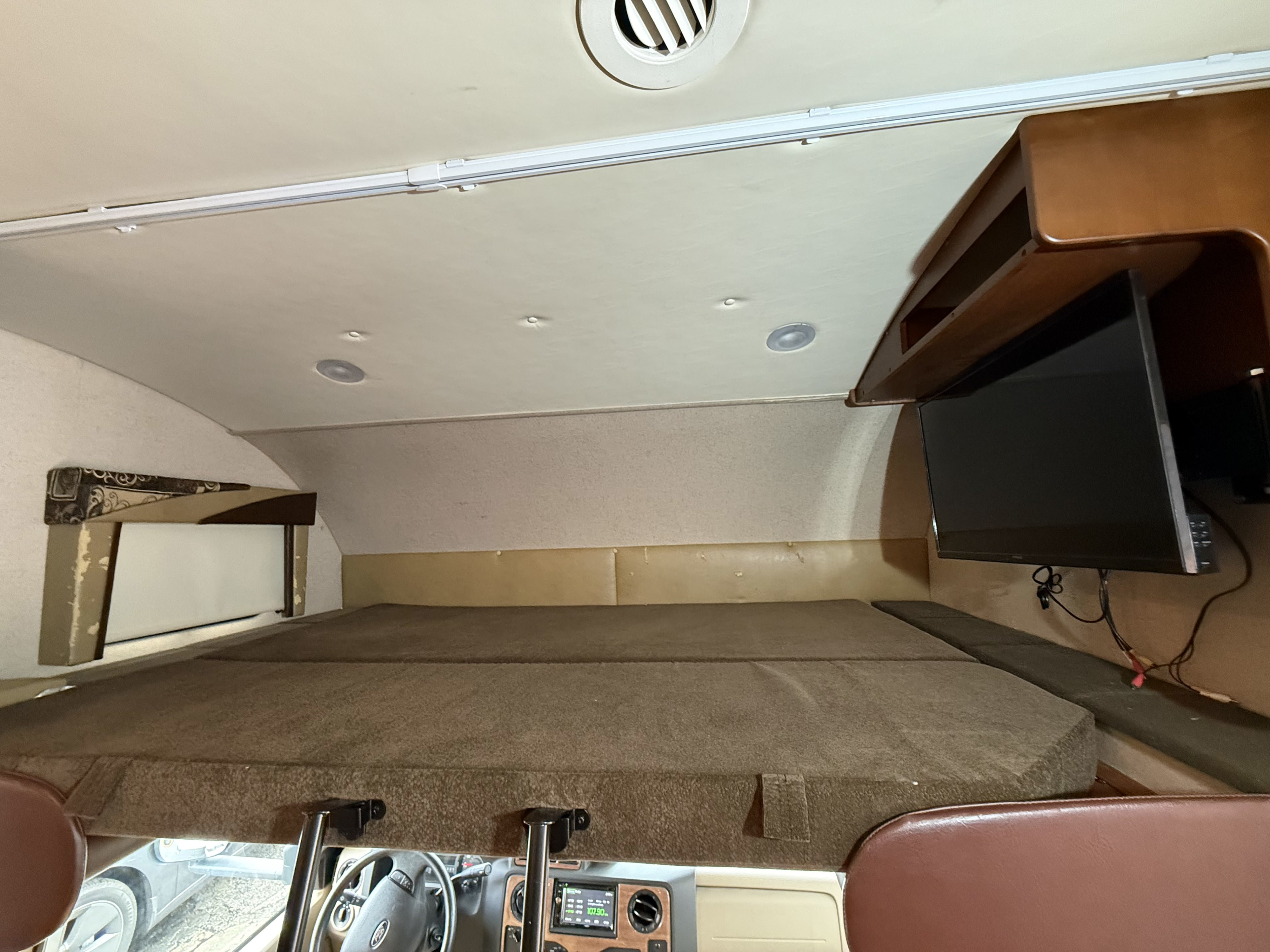 Interior of an RV rental: a spacious overhead bunk bed, TV, ceiling vent, and dashboard view from above.. Jayco Greyhawk 2015