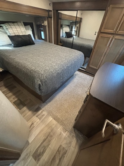 RV rental bedroom features a queen bed with gray bedding, plaid pillows, mirrored closet doors, and mixed carpet/wood flooring.. Keystone RV Sprinter 2019